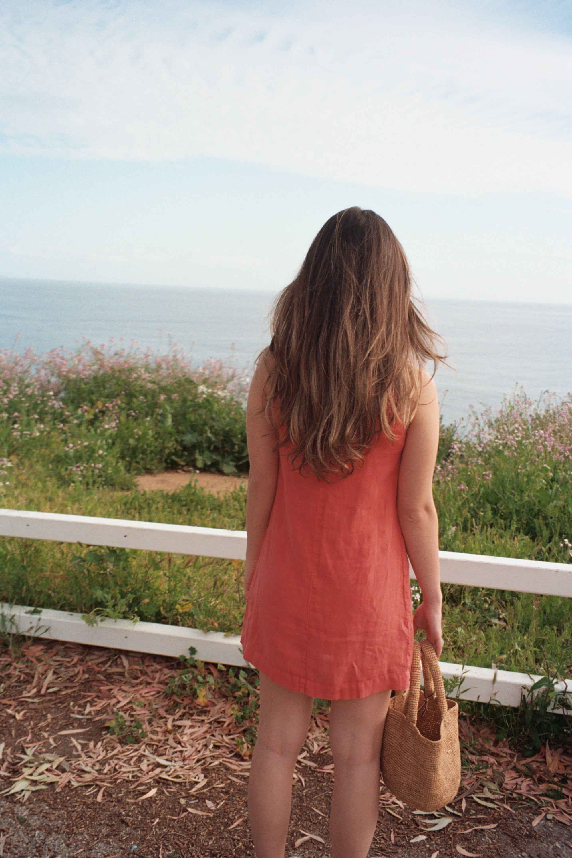 Female model wearing sustainable orange 100% linen dress with a simple and comfortable silhouette overlooking the ocean- VIR VITA
#color_cayenne