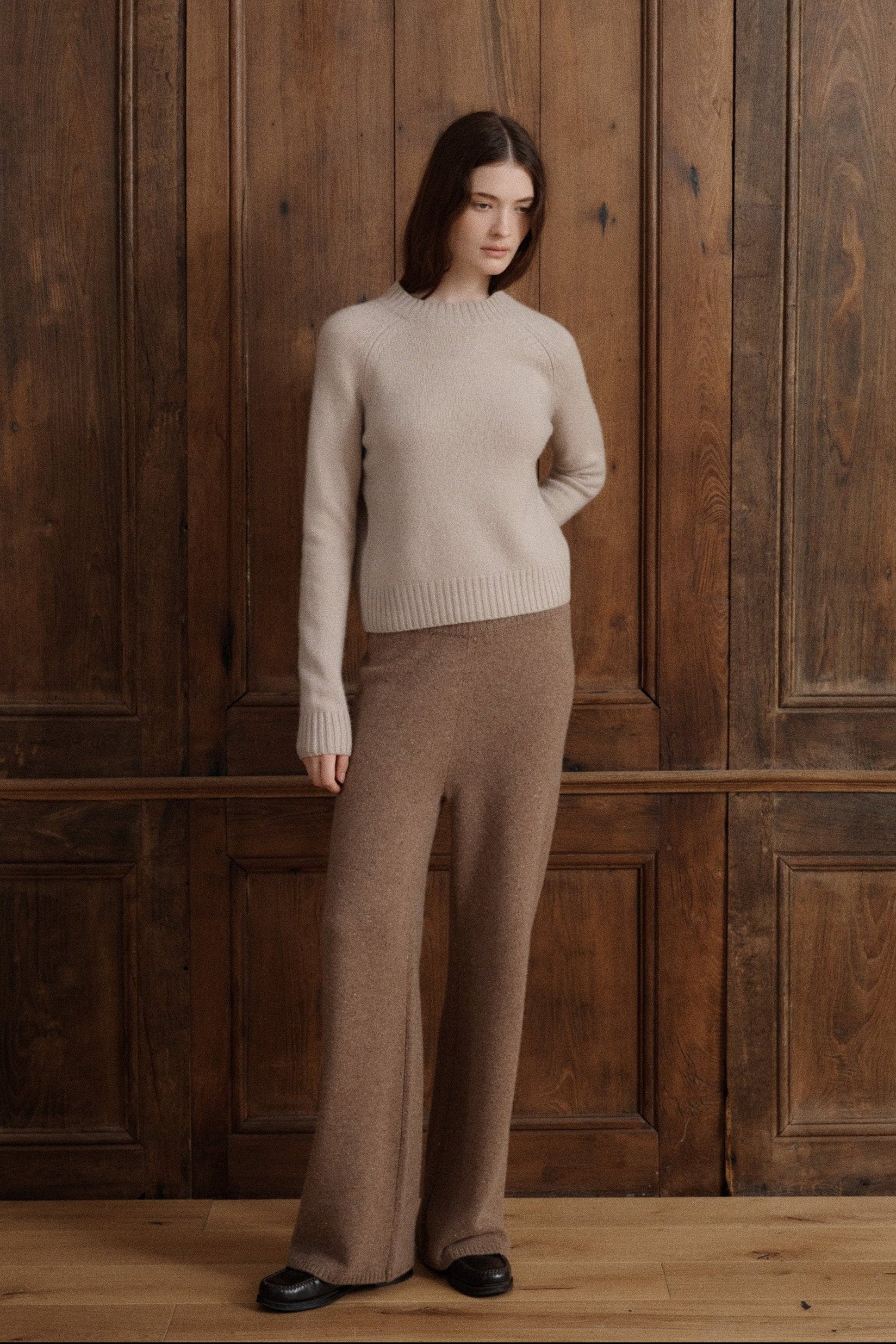 Female model posing in a classic mock neck raglan sleeve cashmere fitted sweater in a soft nuetral beige color. Crafted in cashmere with a ribbed hem that sits at the waist. The sweater is paired with cashmere lounge pants in a light brown and black loafers.
#color_claystone