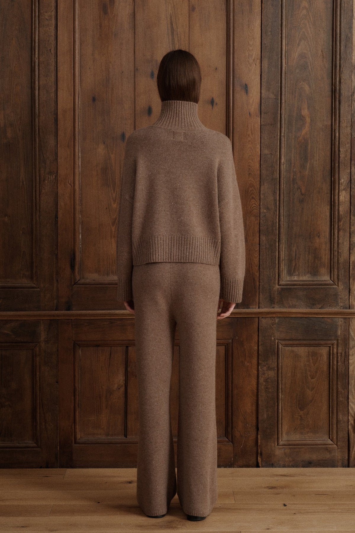 Female model wearing a turtleneck jumper knit in Grade A cashmere in a soft speckled brown color. It features wide balloon sleeves and dropped shoulders for an effortless silhouette. It is paired with matching lounge cashmere pants and black loafers. - VIR VITA
#color_toasted walnut