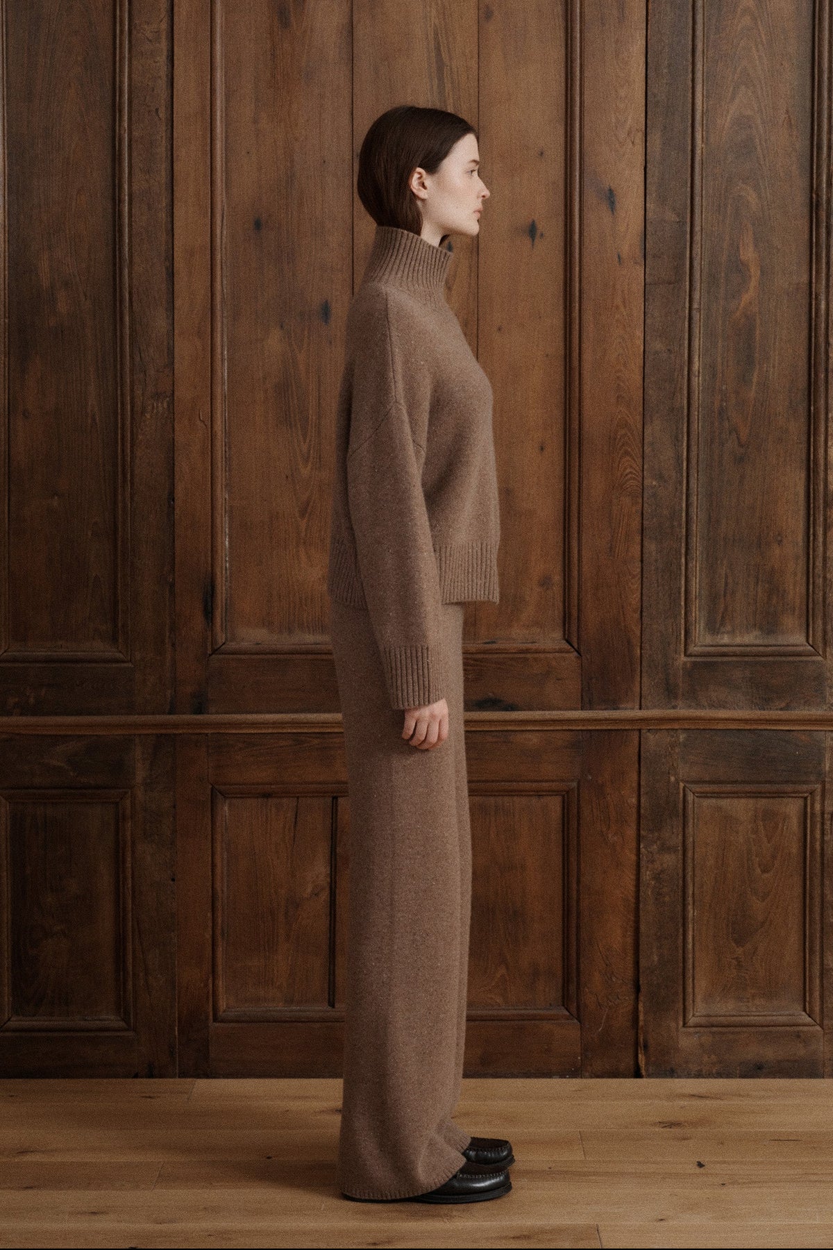 Female model wearing a turtleneck jumper knit in Grade A cashmere in a soft speckled brown color. It features wide balloon sleeves and dropped shoulders for an effortless silhouette. It is paired with matching lounge cashmere pants and black loafers. - VIR VITA
#color_toasted walnut