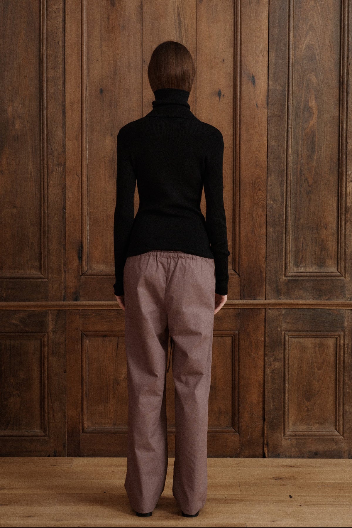 Female model posing wearing a black fitted turtleneck crafted from a fine wool, cashmere and silk blend. Paired with cotton poplin drawstring pants in brown and black flats. - VIR VITA
#color_black