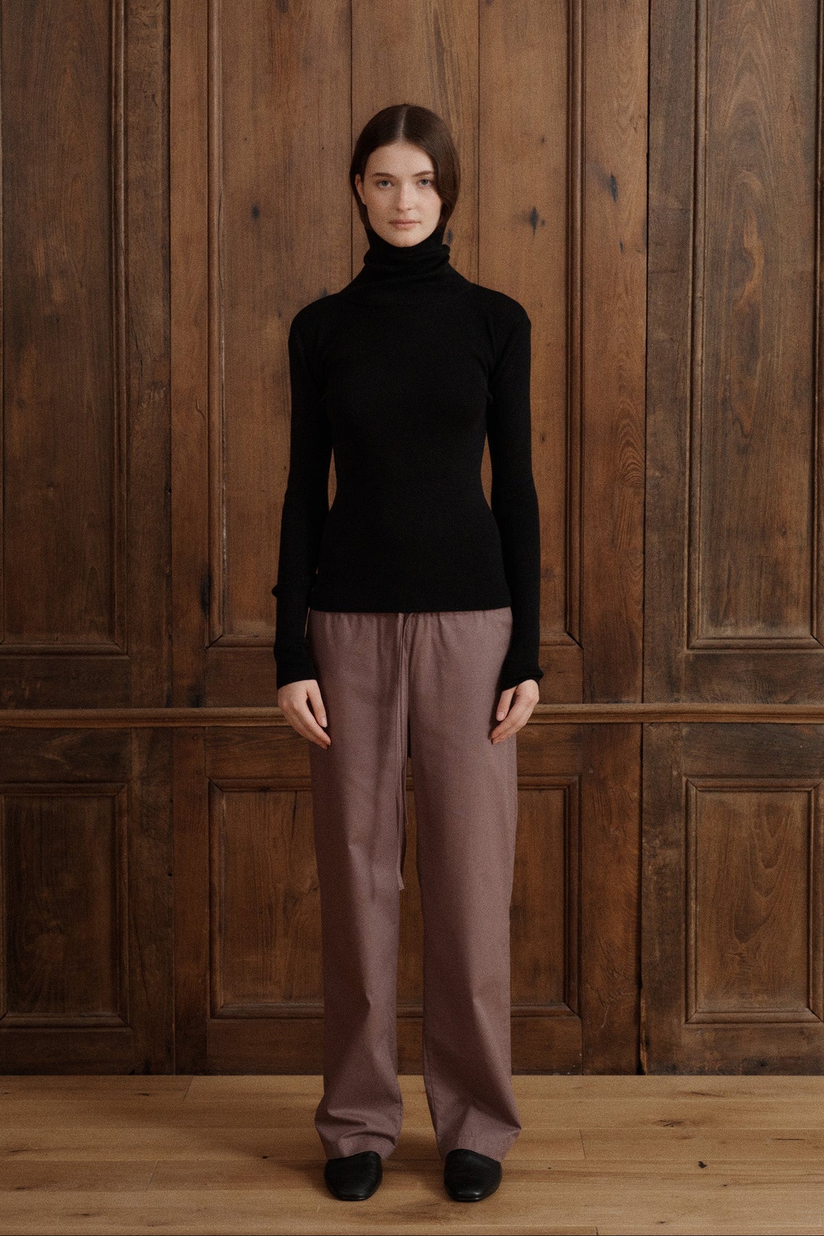 Female model posing wearing a black fitted turtleneck crafted from a fine wool, cashmere and silk blend. Paired with cotton poplin drawstring pants in brown and black flats. - VIR VITA
#color_black