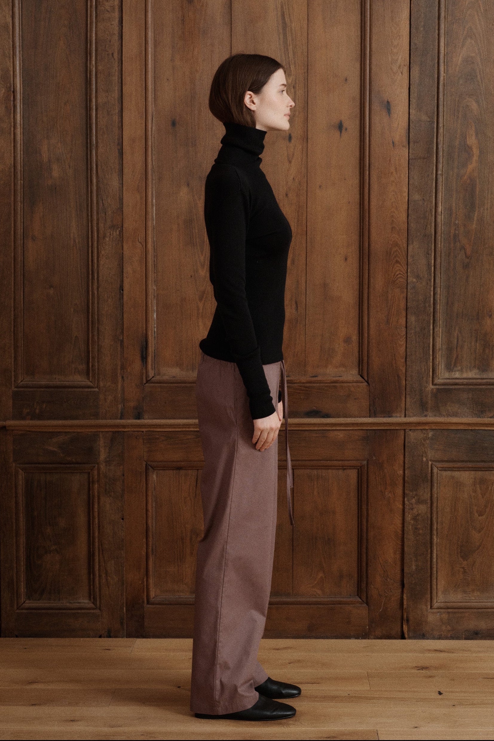 Female model posing wearing a black fitted turtleneck crafted from a fine wool, cashmere and silk blend. Paired with cotton poplin drawstring pants in brown and black flats. - VIR VITA
#color_black
