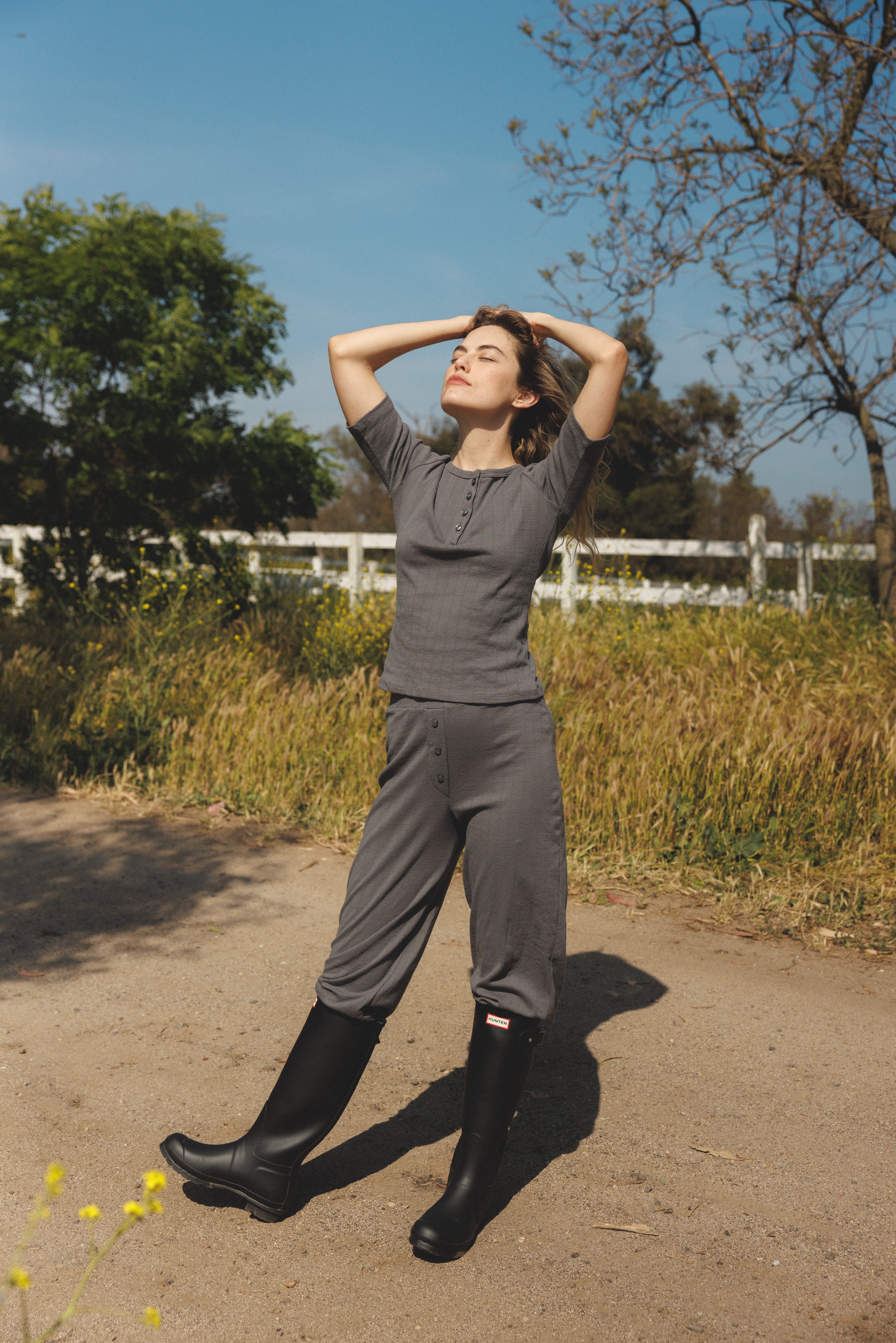 Female model wearing a grey henley quarter sleeve cotton pointelle top with matching buttons paired with cotton pointelle lounge pants in grey and tall black boots - VIR VITA
#color_stone grey