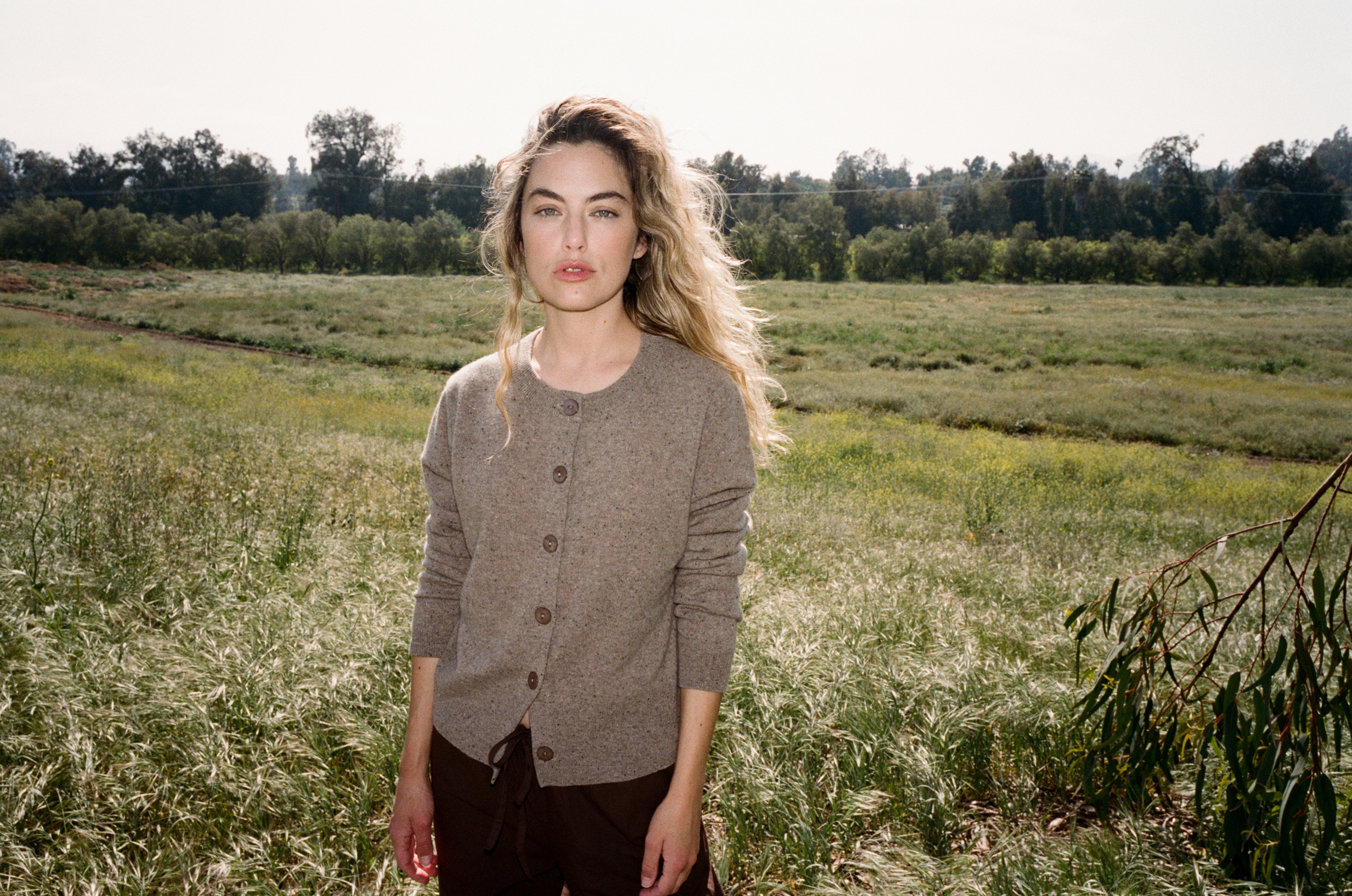 Female model standing in a field wearing a light brown ultra-soft luxurious cashmere button up cardigan paired with dark brown drawstring pants - VIR VITA
#color_walnut