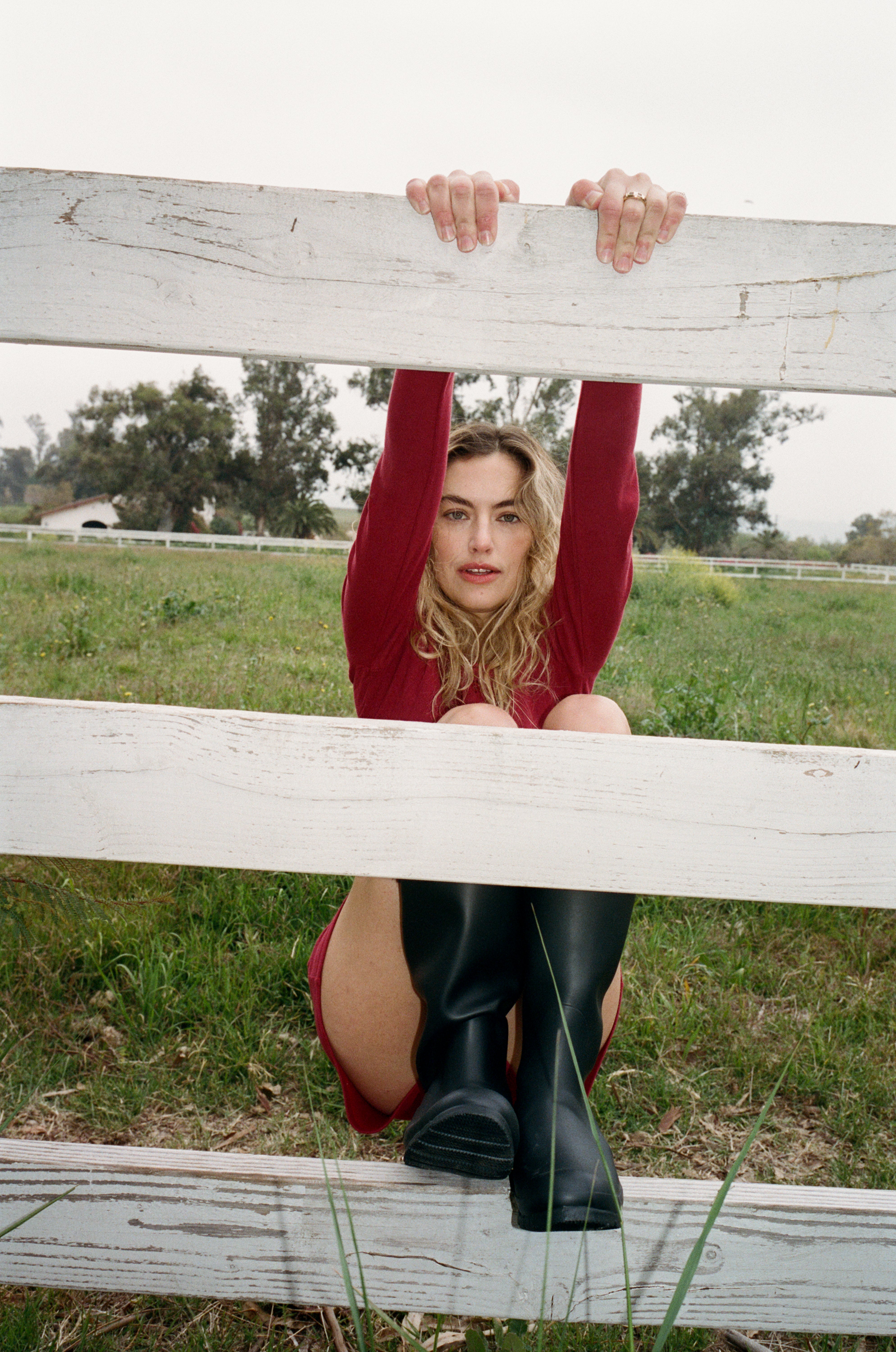 Female model wearing sustainable dark red pointelle lounge shorts made of 100% recycled cotton featuring a relaxed fit paired with a matching pointelle henley shirt in dark red and black tall boots leaning against a fence- VIR VITA
#color_sun dried tomato
