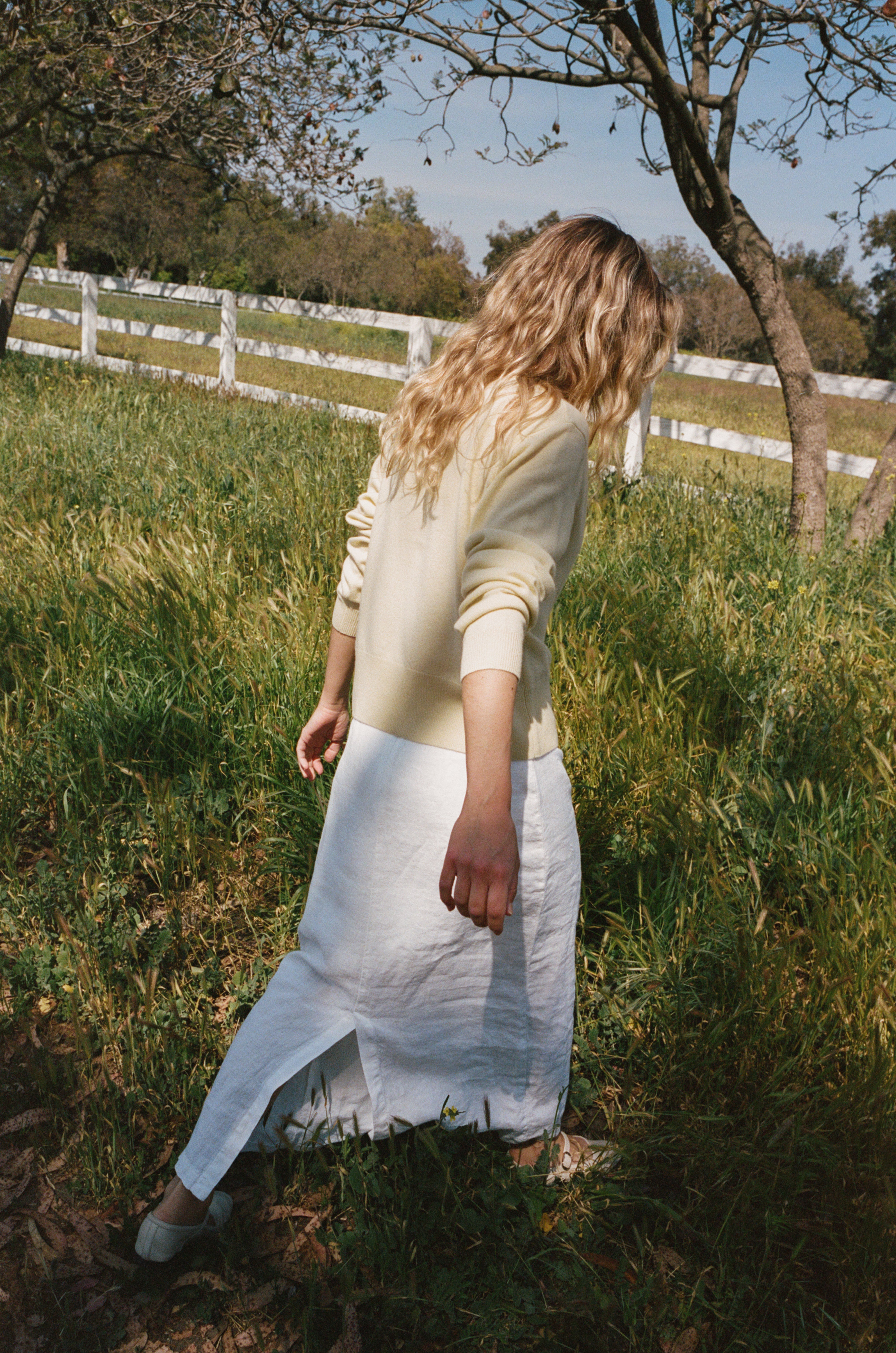 Female model wearing a premium 100% linen maxi skirt featuring a high waisted silhouette in white paired with a pale yellow cashmere cardigan and flats standing in a field of grass- VIR VITA
#color_white