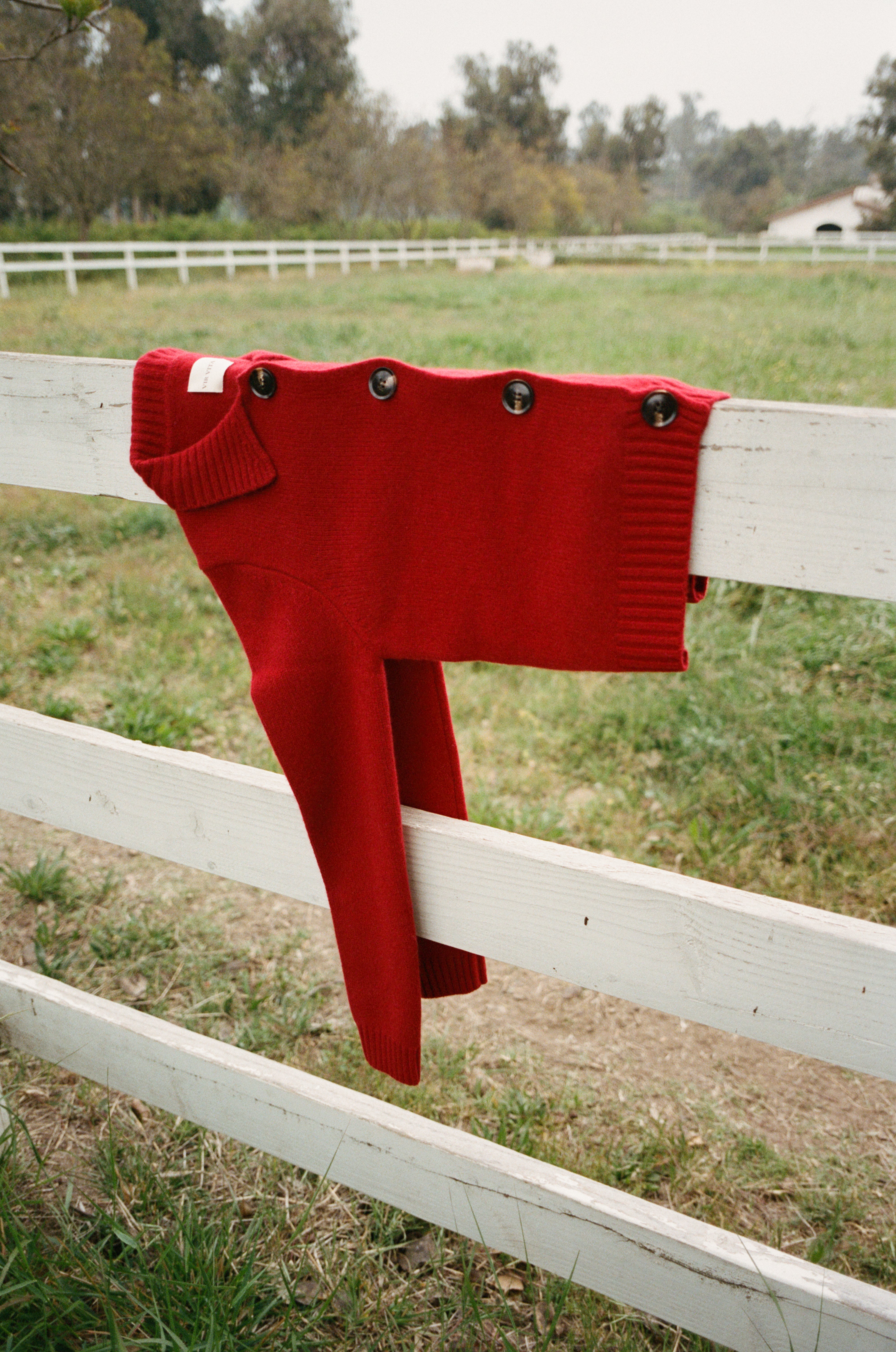 Red ultra-soft luxurious cashmere cardigan featuring a classic silhouette with a collar and large buttons laid over a fence - VIR VITA
#color_cherry