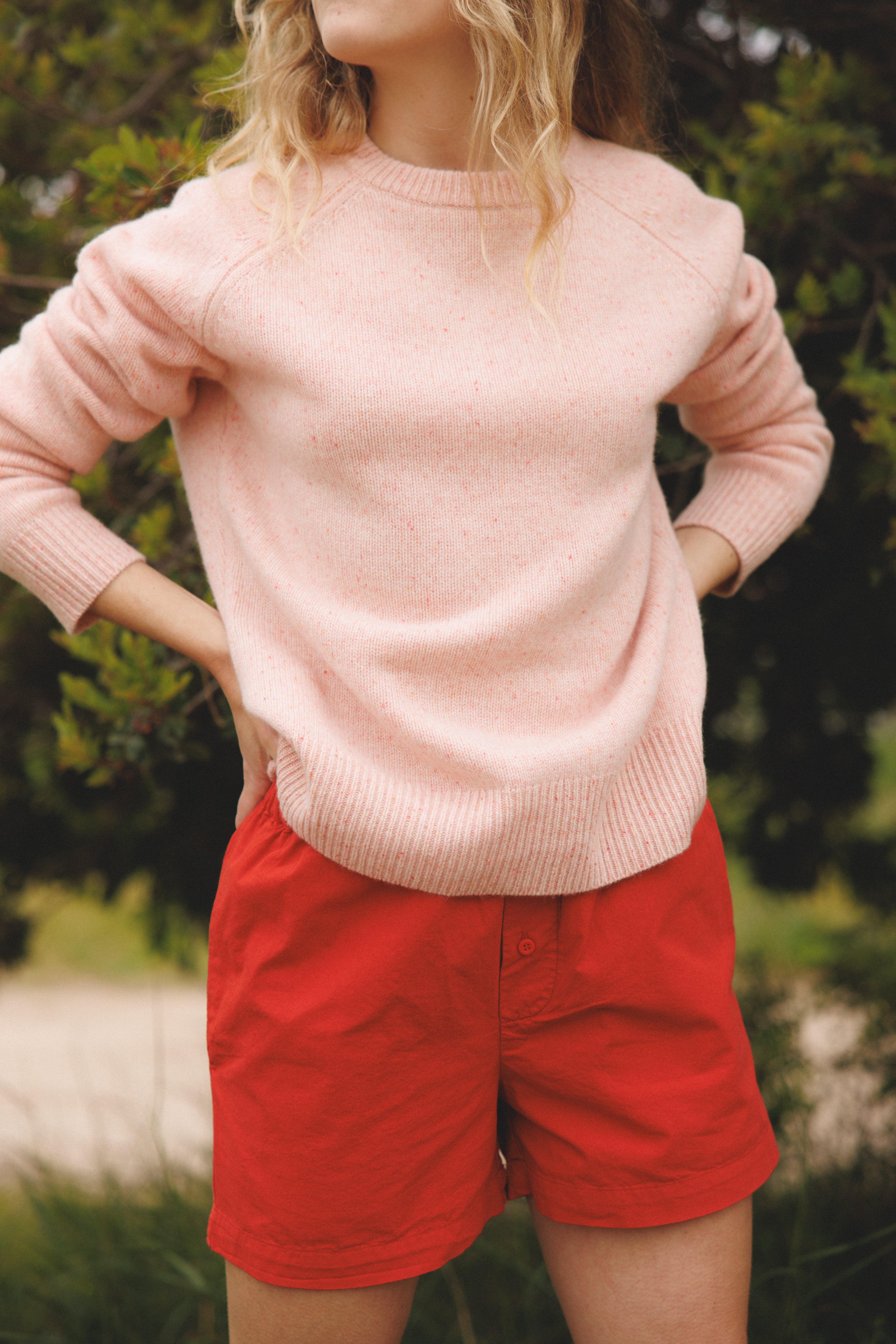 Female model wearing a light pink ultra-soft luxurious cashmere pullover sweater featuring a classic silhouette and raglan sleeves paired with red cotton poplin shorts - VIR VITA
#color_rosewater