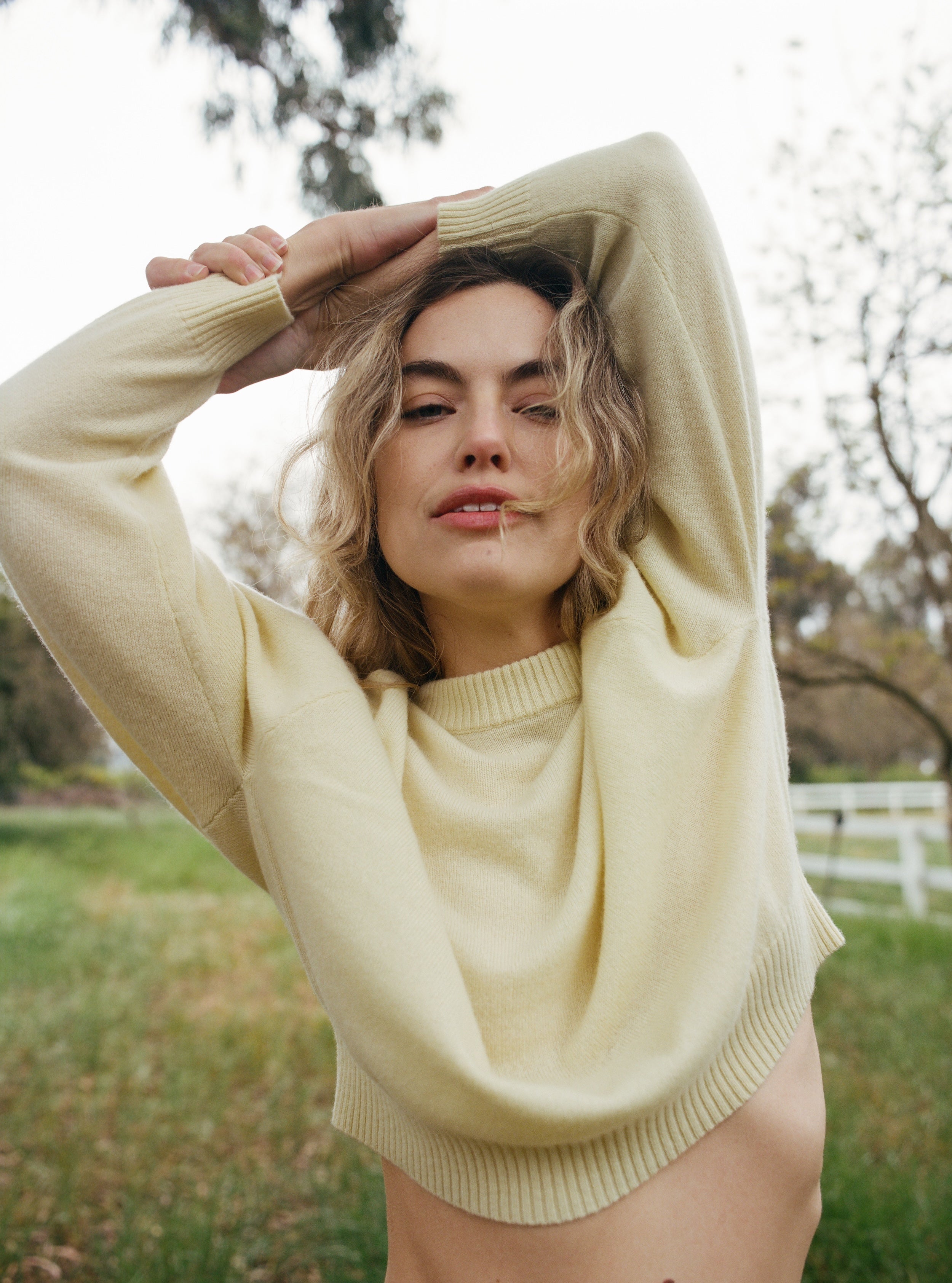 Female model in a field wearing a pale yellow luxurious and soft cashmere pullover sweater with a classic and relaxed silhouette - VIR VITA
#color_butter