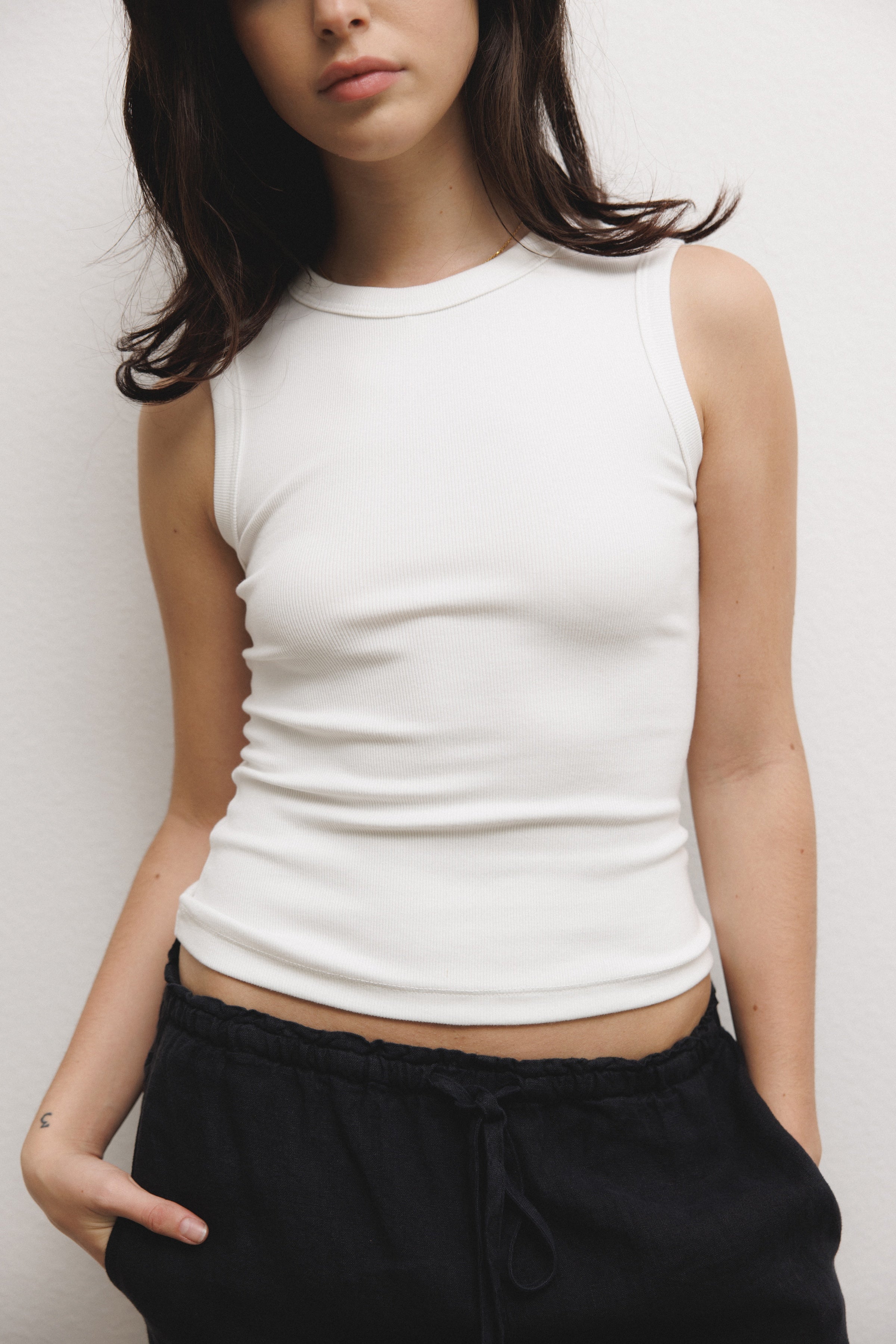 Female model wearing a luxurious supima cotton tank top featuring a fitted silhouette with a high neckline in white paired with 100% linen drawstring pants in black - VIR VITA
#color_white