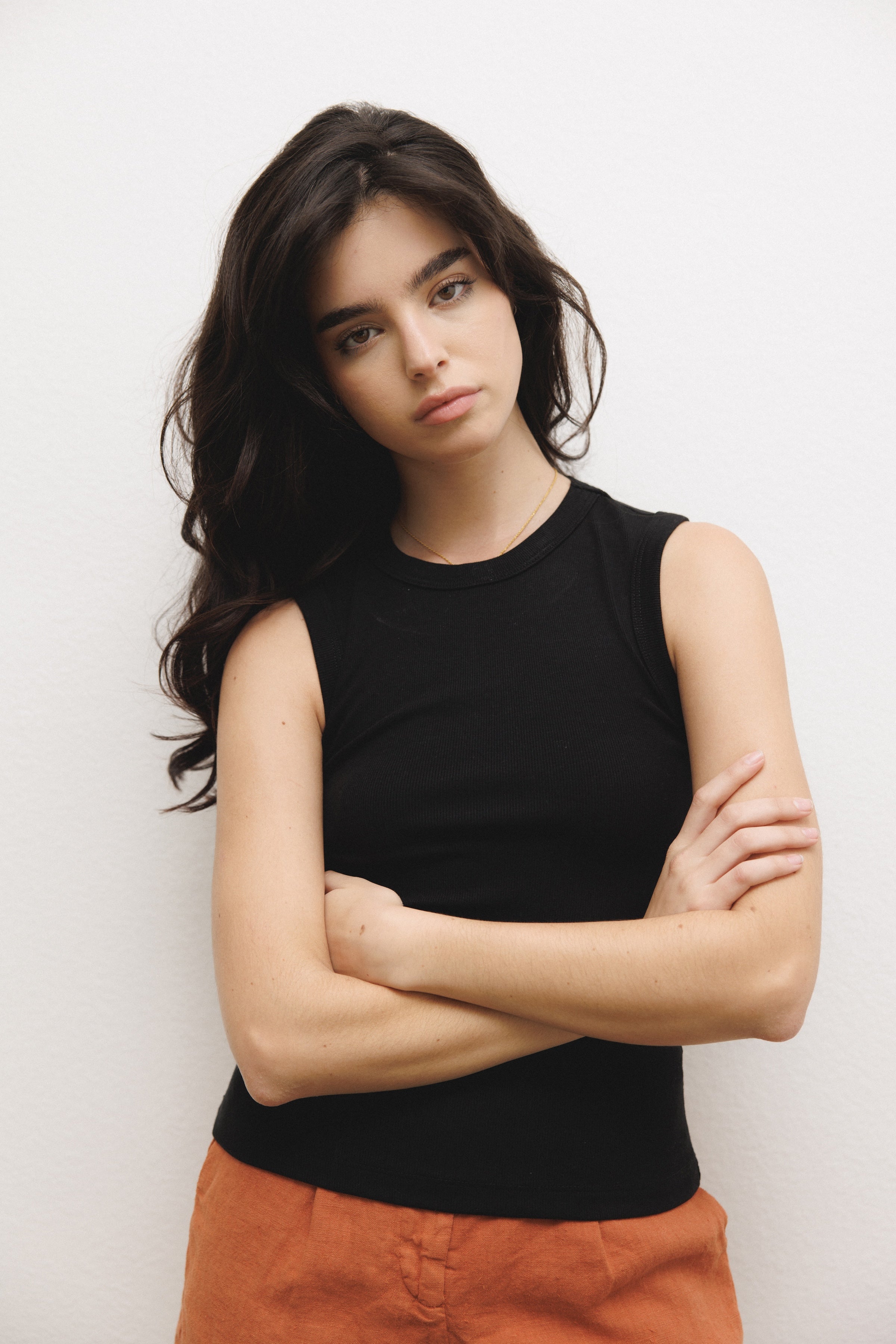 Female model wearing a luxurious supima cotton tank top featuring a fitted silhouette with a high neckline in black paired with 100% linen trousers in orange - VIR VITA
#color_black