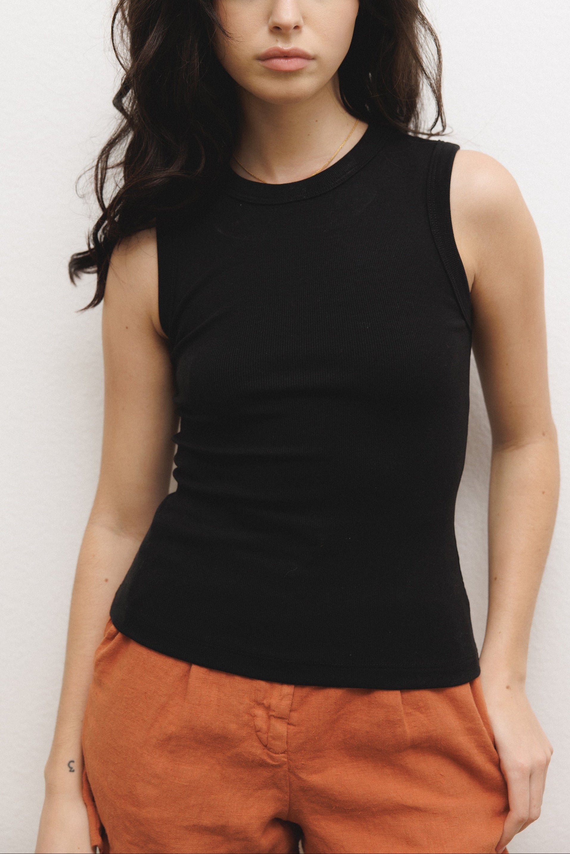 Female model wearing a luxurious supima cotton tank top featuring a fitted silhouette with a high neckline in black paired with 100% linen trousers in orange - VIR VITA
#color_black