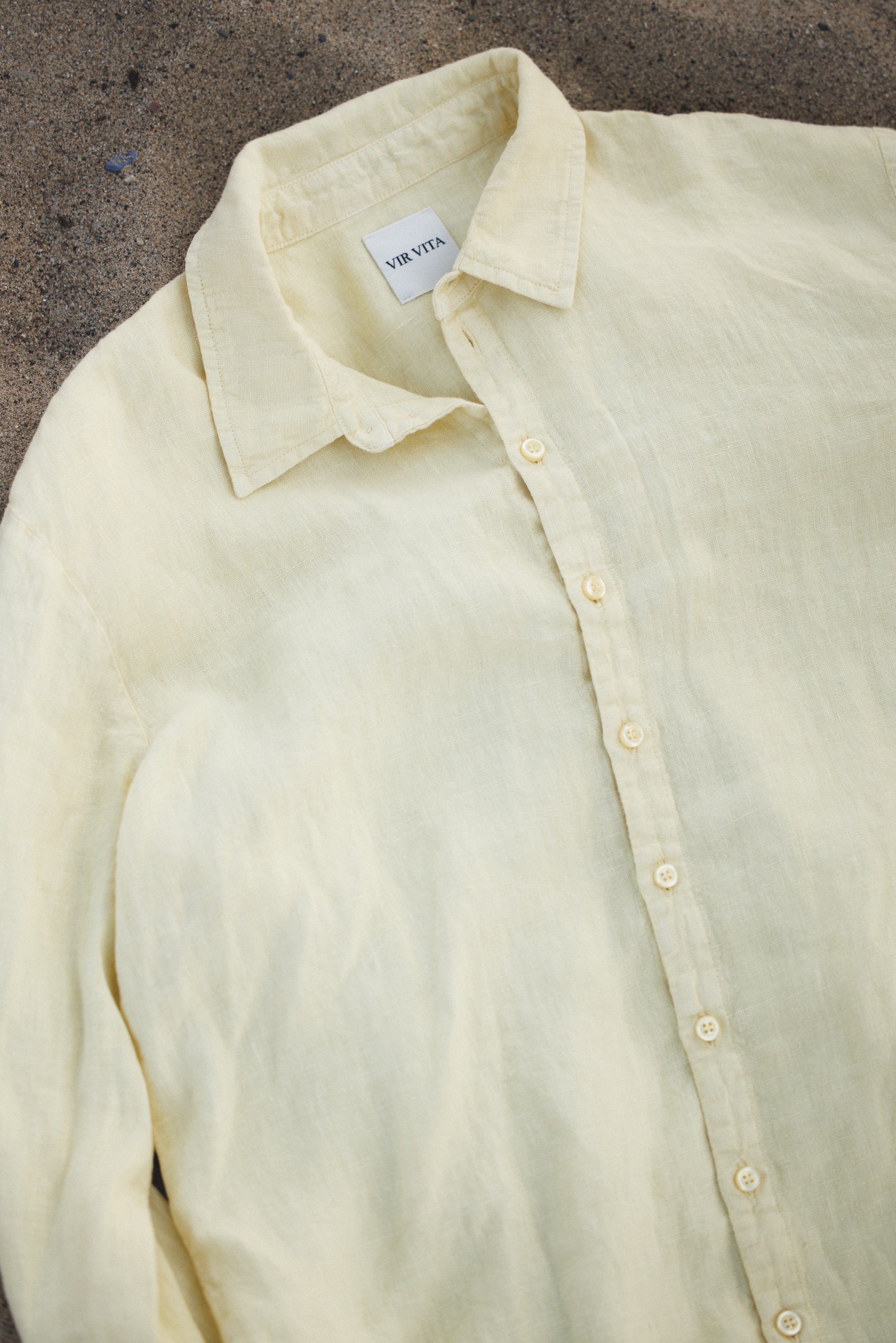 Pale yellow sustainable oversized 100% linen button down long sleeve laid out in sand- VIR VITA #color_butter