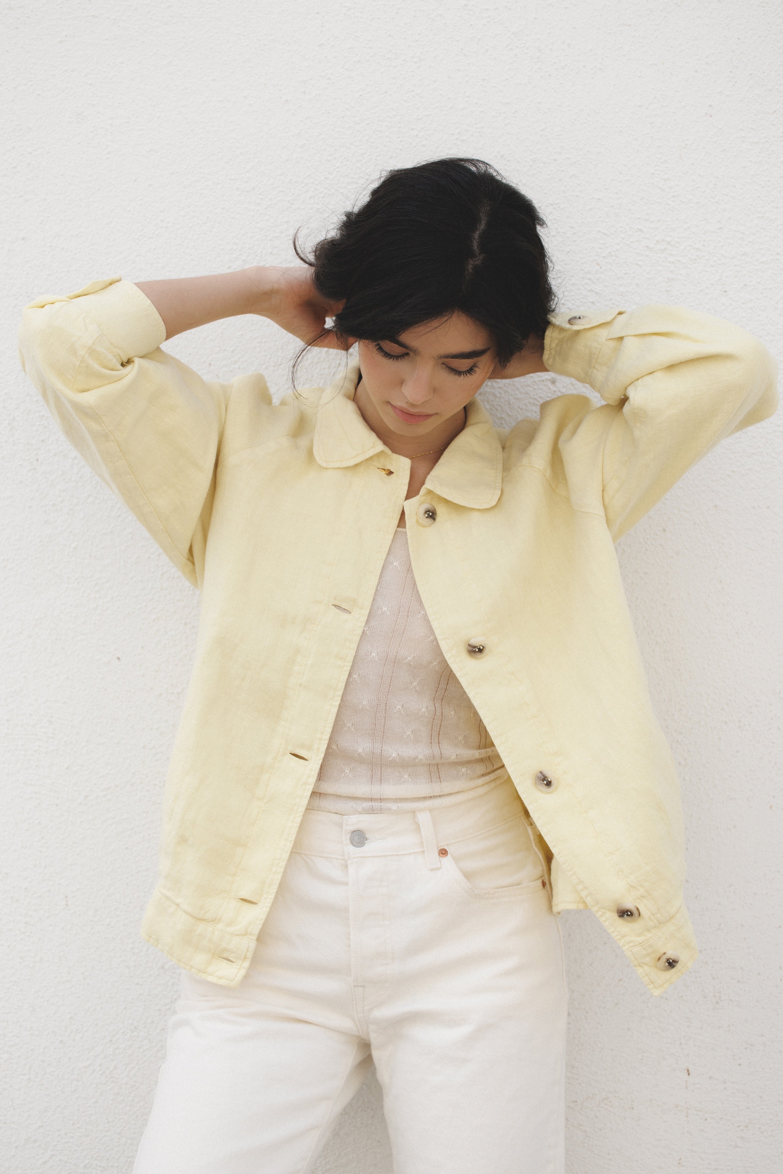 Female model wearing a sustainable butter yellow 100% linen barn jacket with a white cashmere top and white jeans - VIR VITA
#color_butter