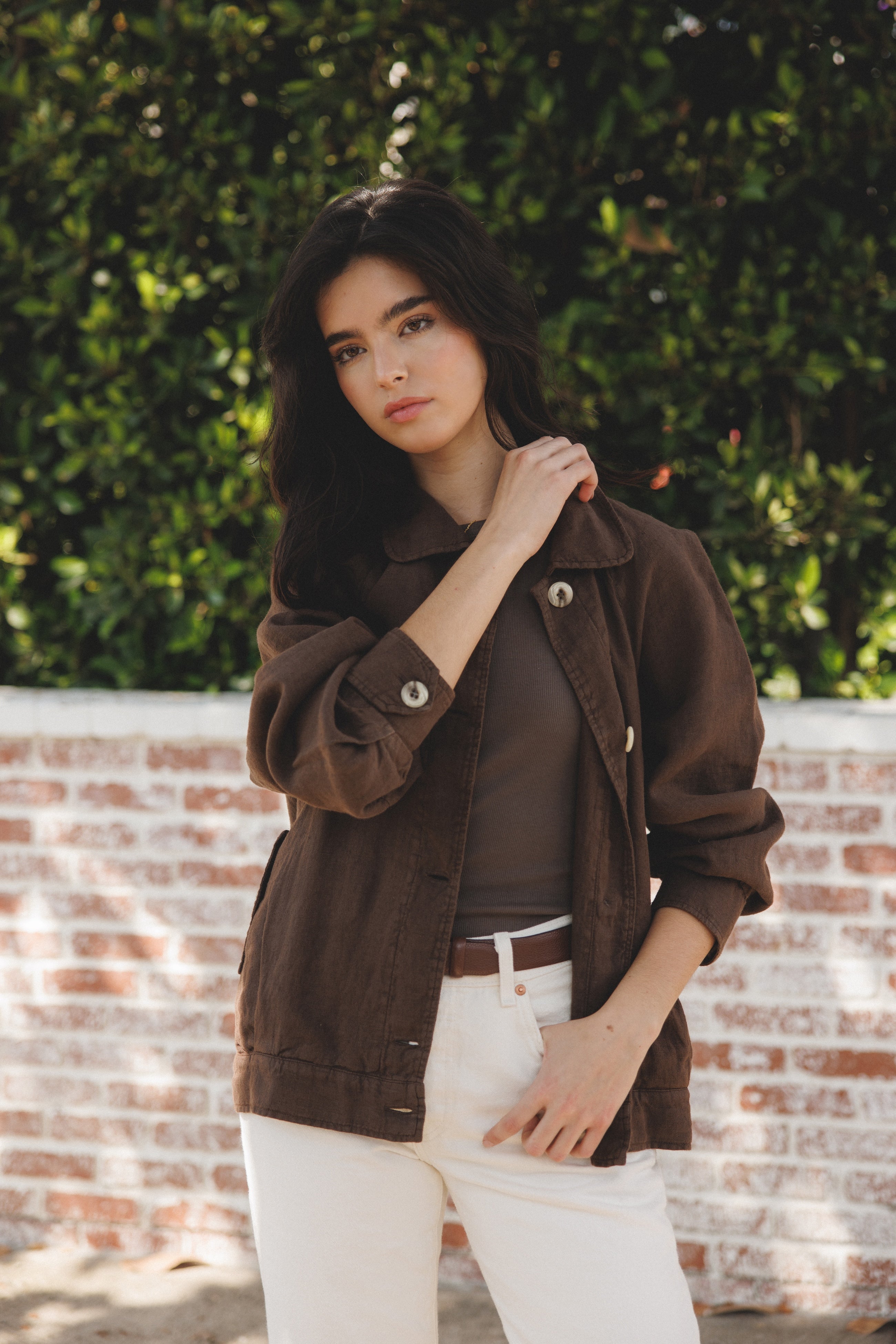 Female model wearing sustainable brown 100% linen barn jacket with brown tank top, white jeans and brown leather belt - VIR VITA
#color_chestnut