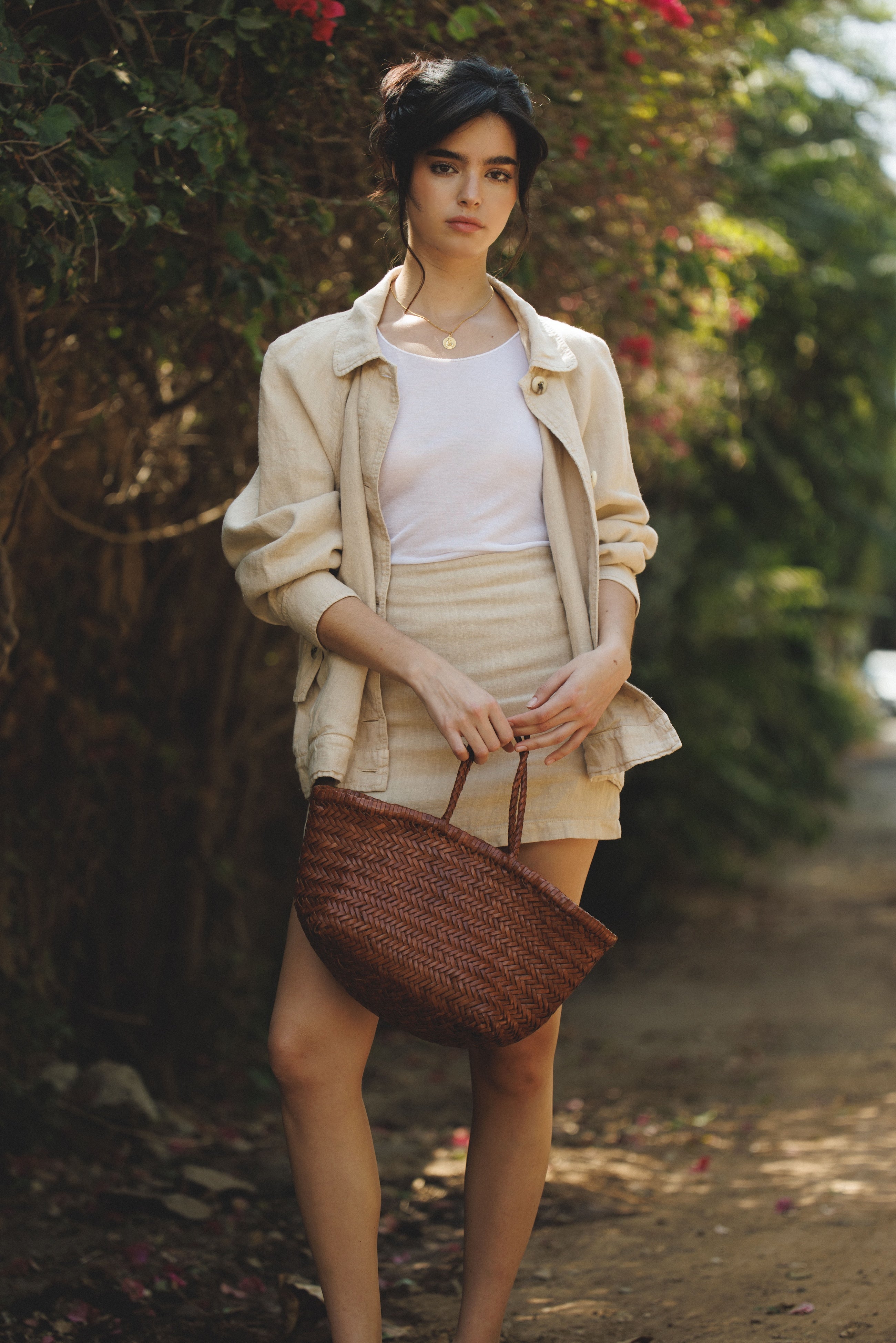 Female model wearing a 100% linen mini skirt with an A-line silhouette in beige paired with a beige 100% linen barn jacket and white tank top holding a brown woven bag - VIR VITA
#color_beige