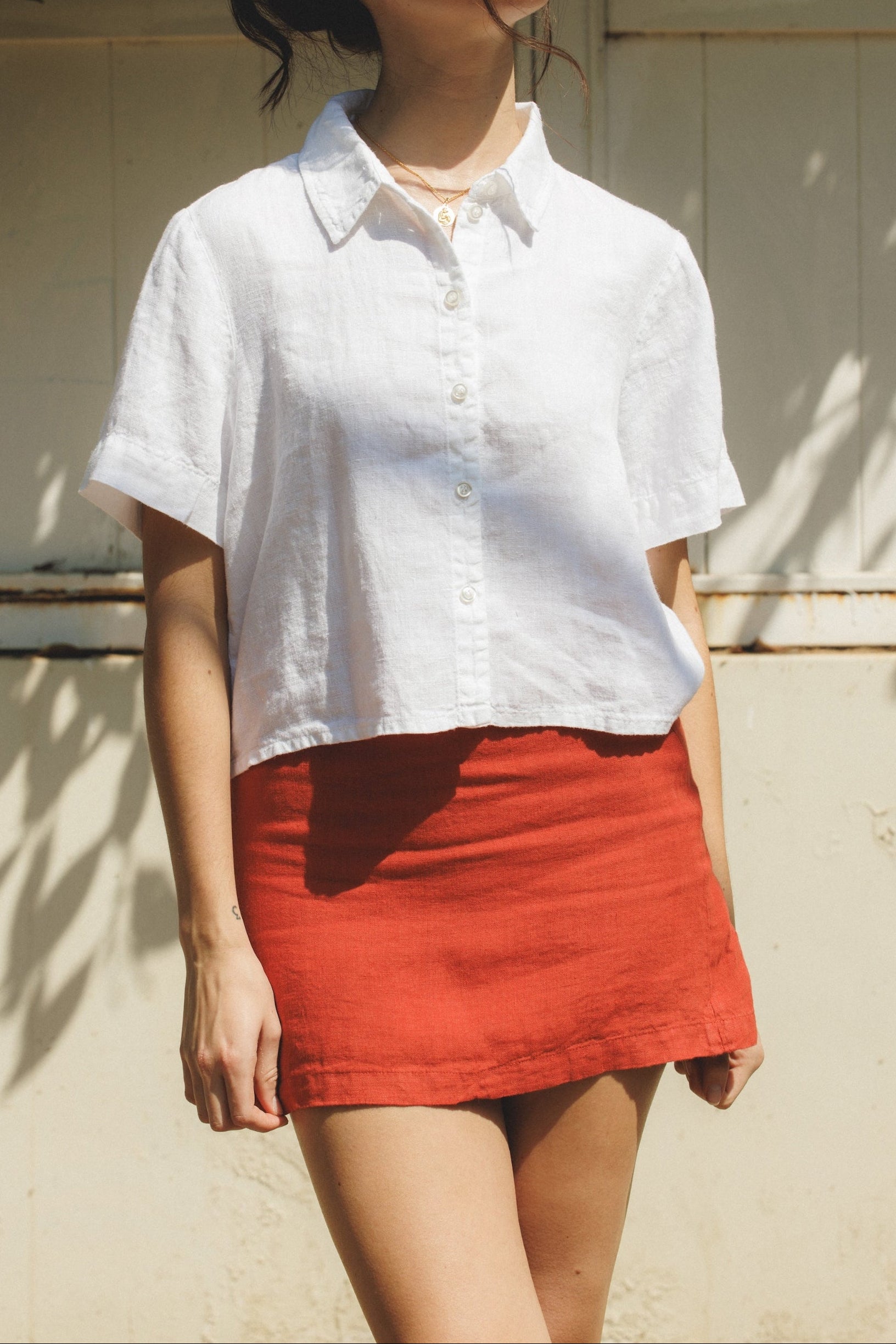 Female model wearing a 100% linen mini skirt with an A-line silhouette in red paired with a white button up short sleeve linen shirt- VIR VITA
#color_apple red