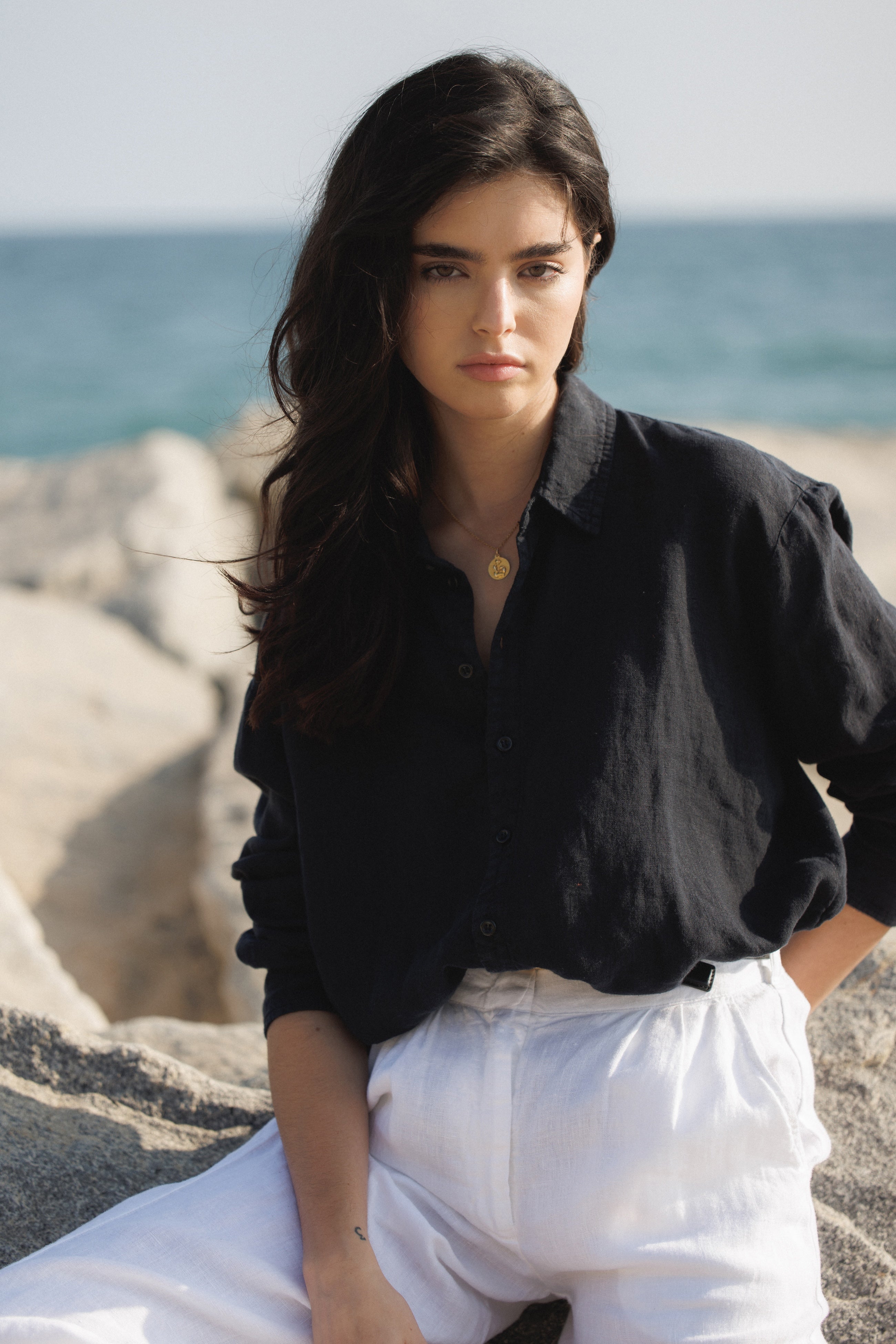 Female model, wearing a black colored sustainable oversized 100% linen button down long sleeve with white linen trousers at the beach- VIR VITA
#color_black