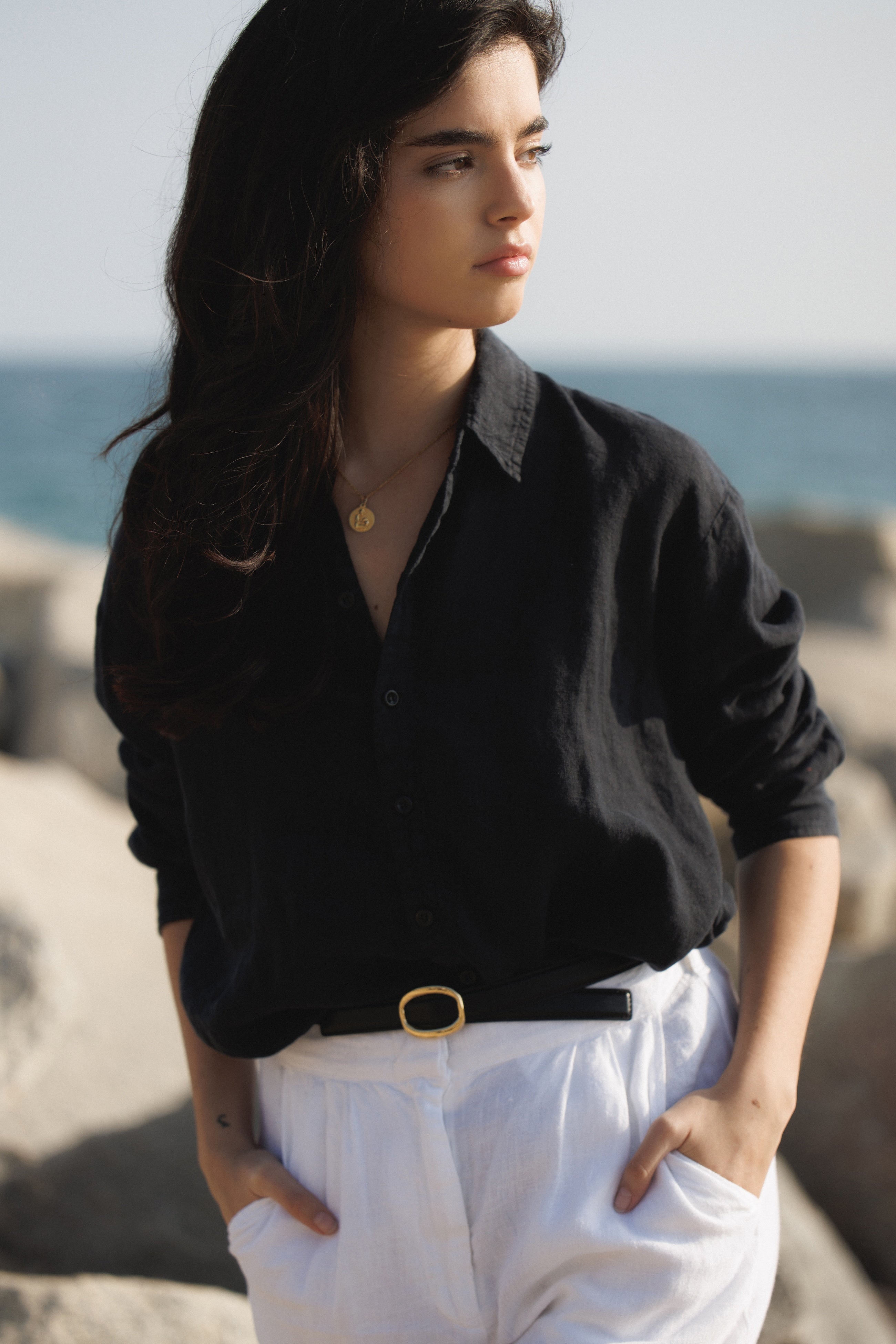 Female model, wearing a black colored sustainable oversized 100% linen button down long sleeve with white linen trousers and black belt at the beach- VIR VITA
#color_black