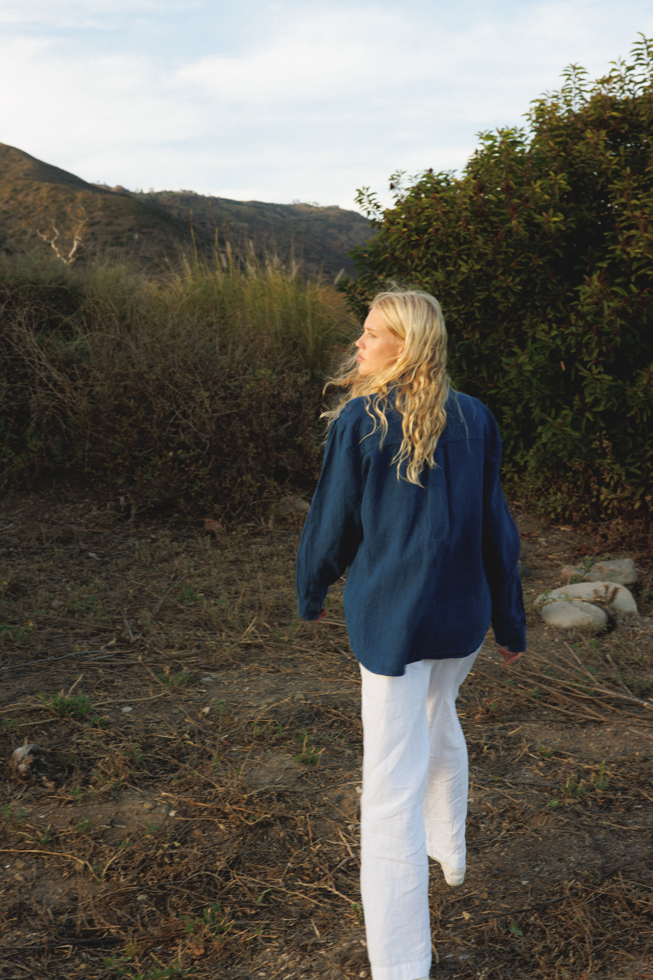 Female model wearing a 100% linen trouser featuring a high waisted double pleat silhouette in white paired with a 100% linen button up shirt in navy blue - VIR VITA
#color_white