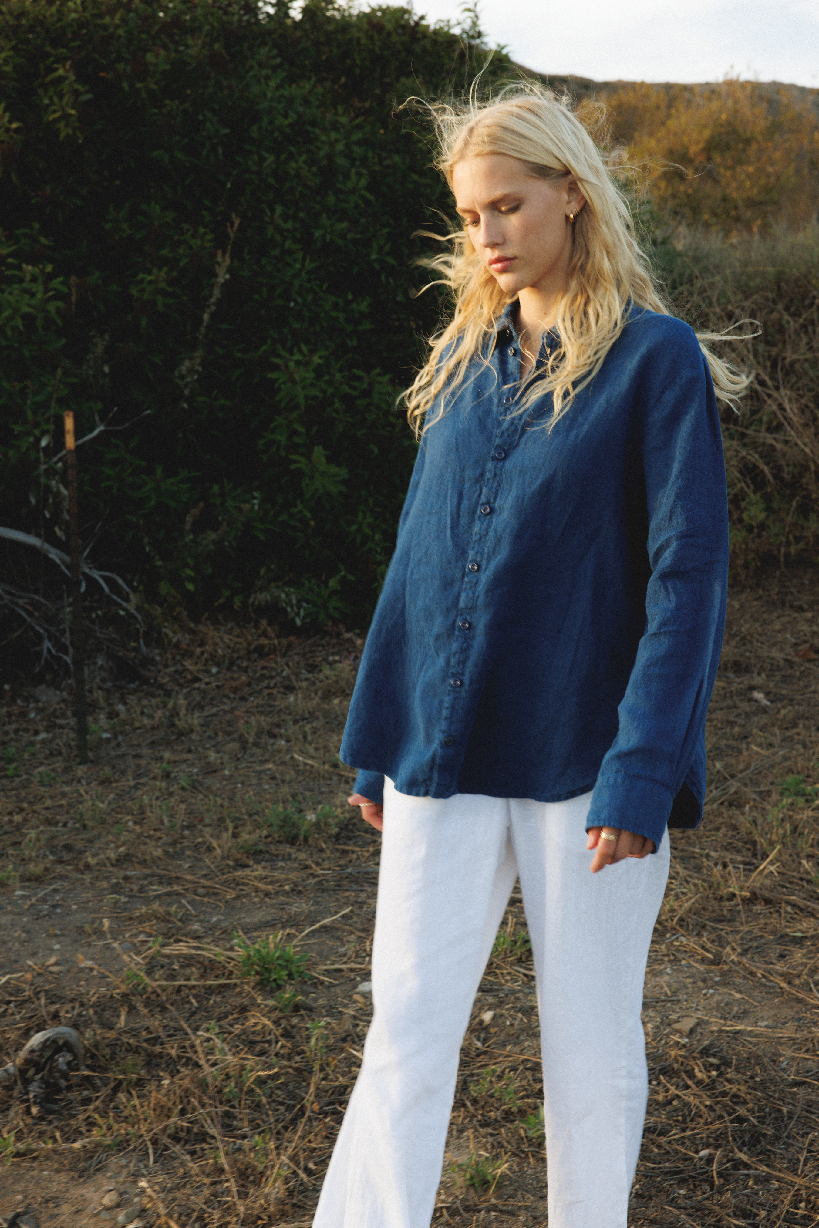 Female model wearing a 100% linen trouser featuring a high waisted double pleat silhouette in white paired with a 100% linen button up shirt in navy blue - VIR VITA
#color_white