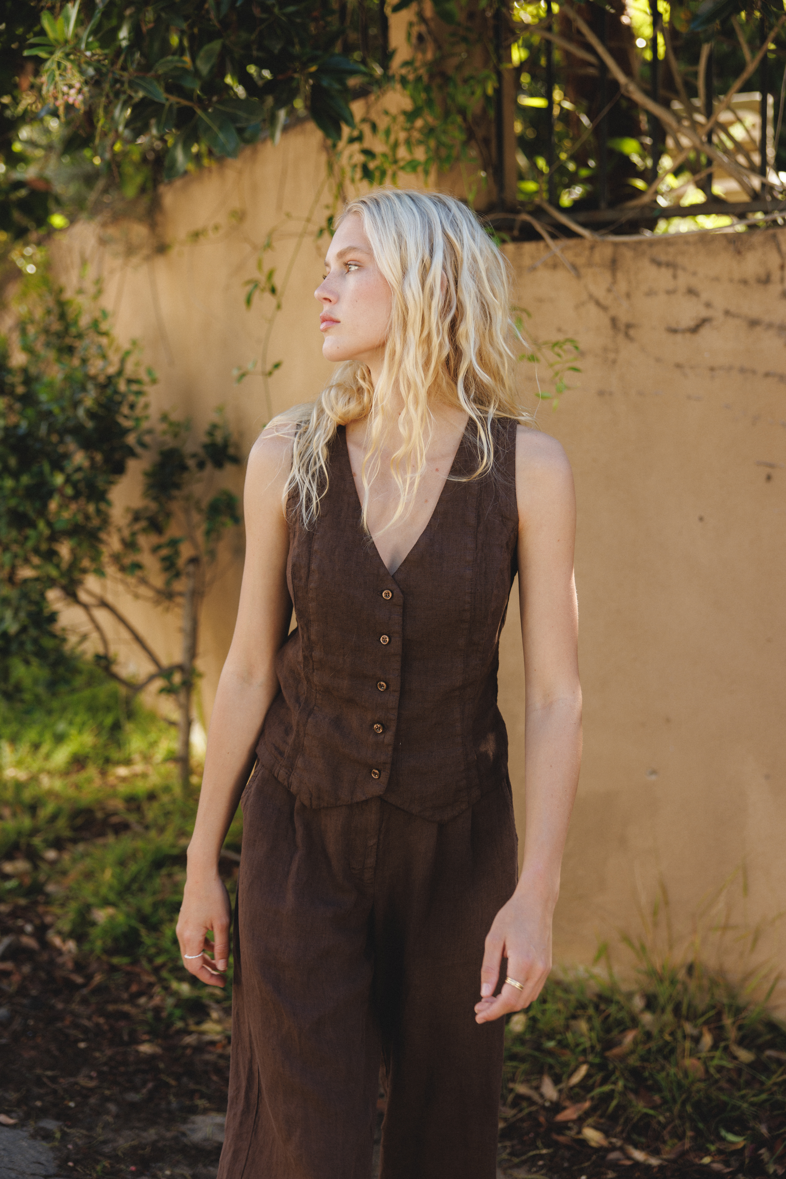 Female model wearing a dark brown sustainable 100% linen vest with matching Italian handcrafted buttons paired with dark brown linen trousers - VIR VITA
#color_chestnut