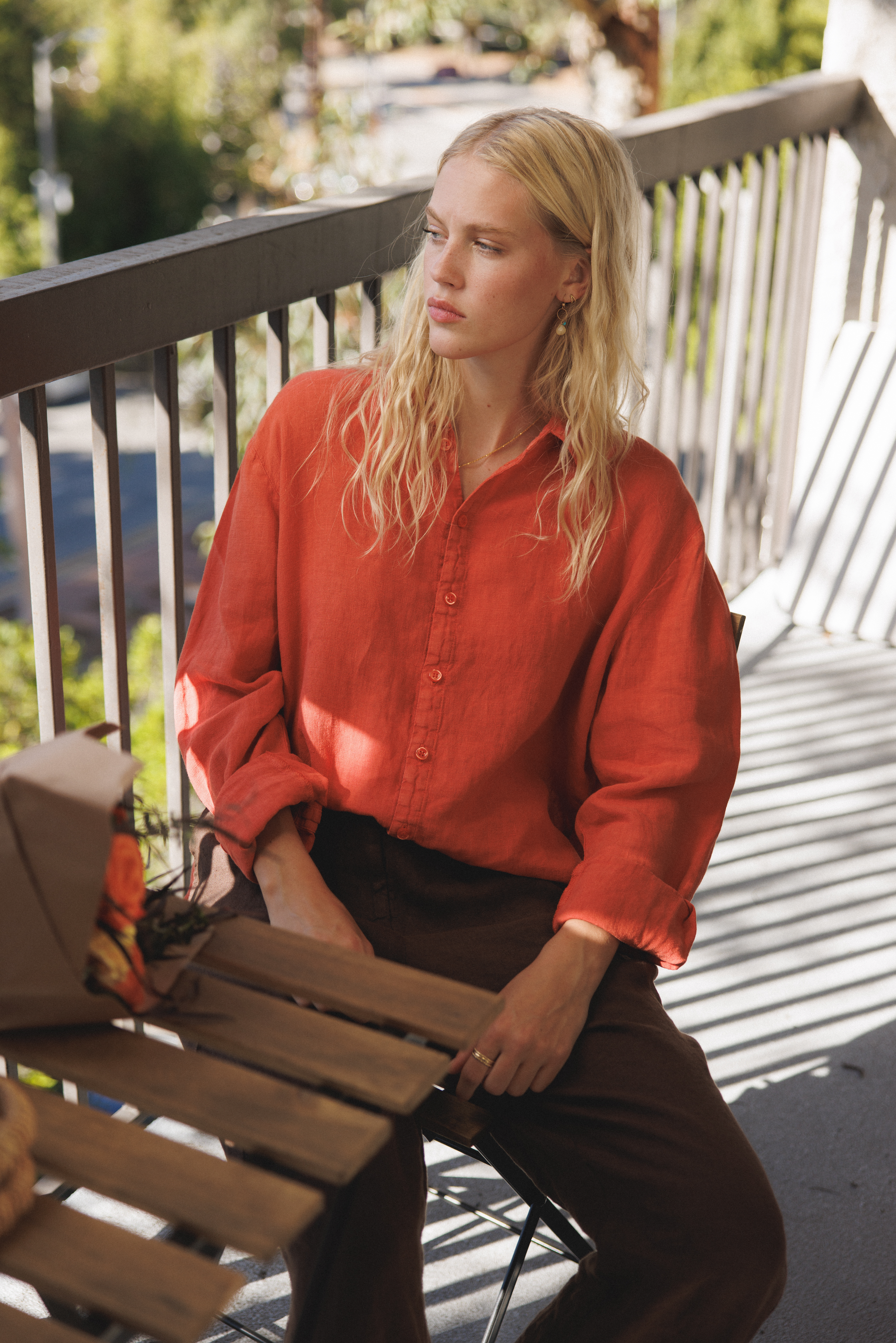 Female model, sitting on a balcony, wearing a cayenne / orange colored sustainable oversized 100% linen button down long sleeve paired with dark brown linen pants - VIR VITA
#color_cayenne