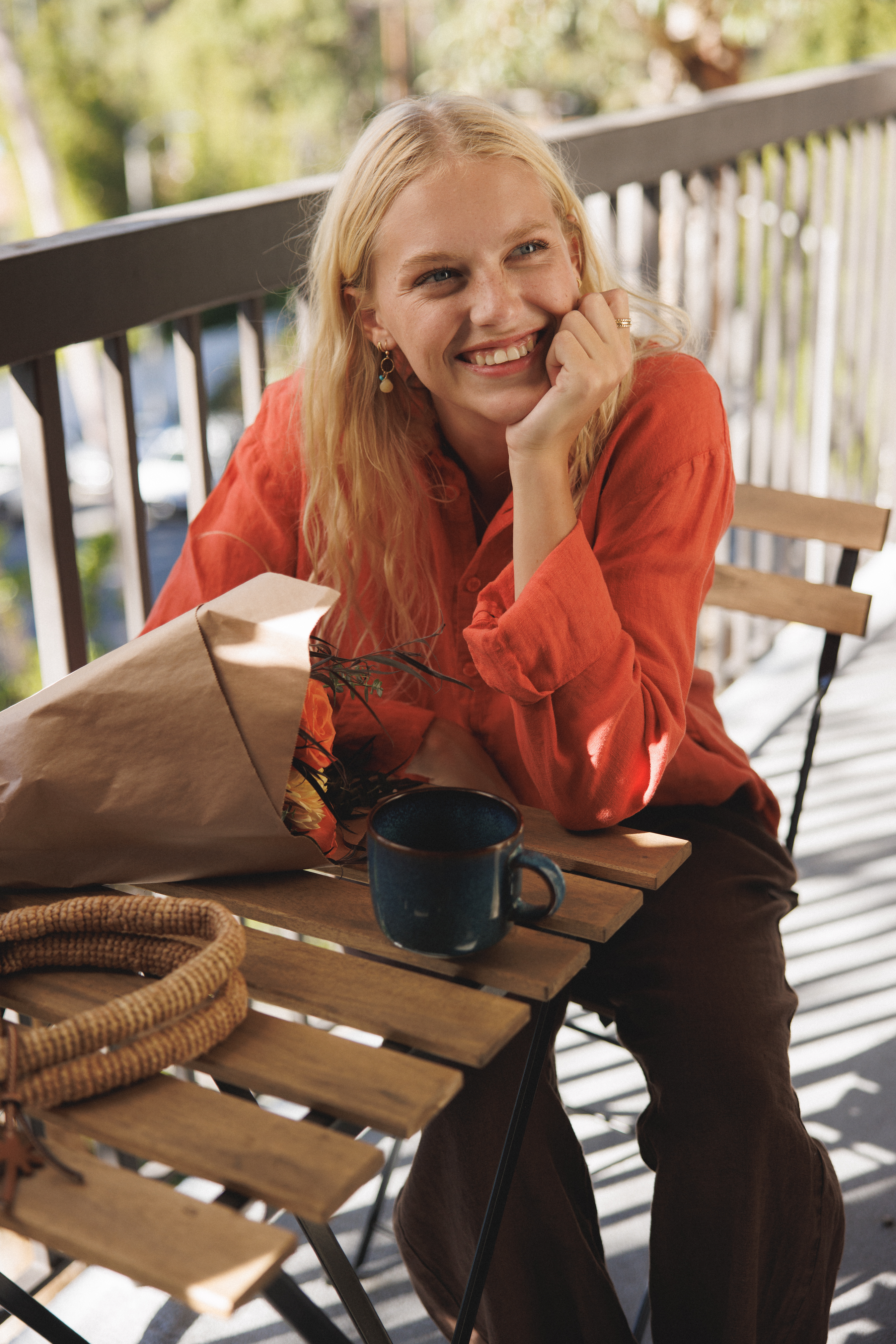Female model, sitting on a balcony, wearing a cayenne / orange colored sustainable oversized 100% linen button down long sleeve paired with dark brown linen pants - VIR VITA
#color_cayenne