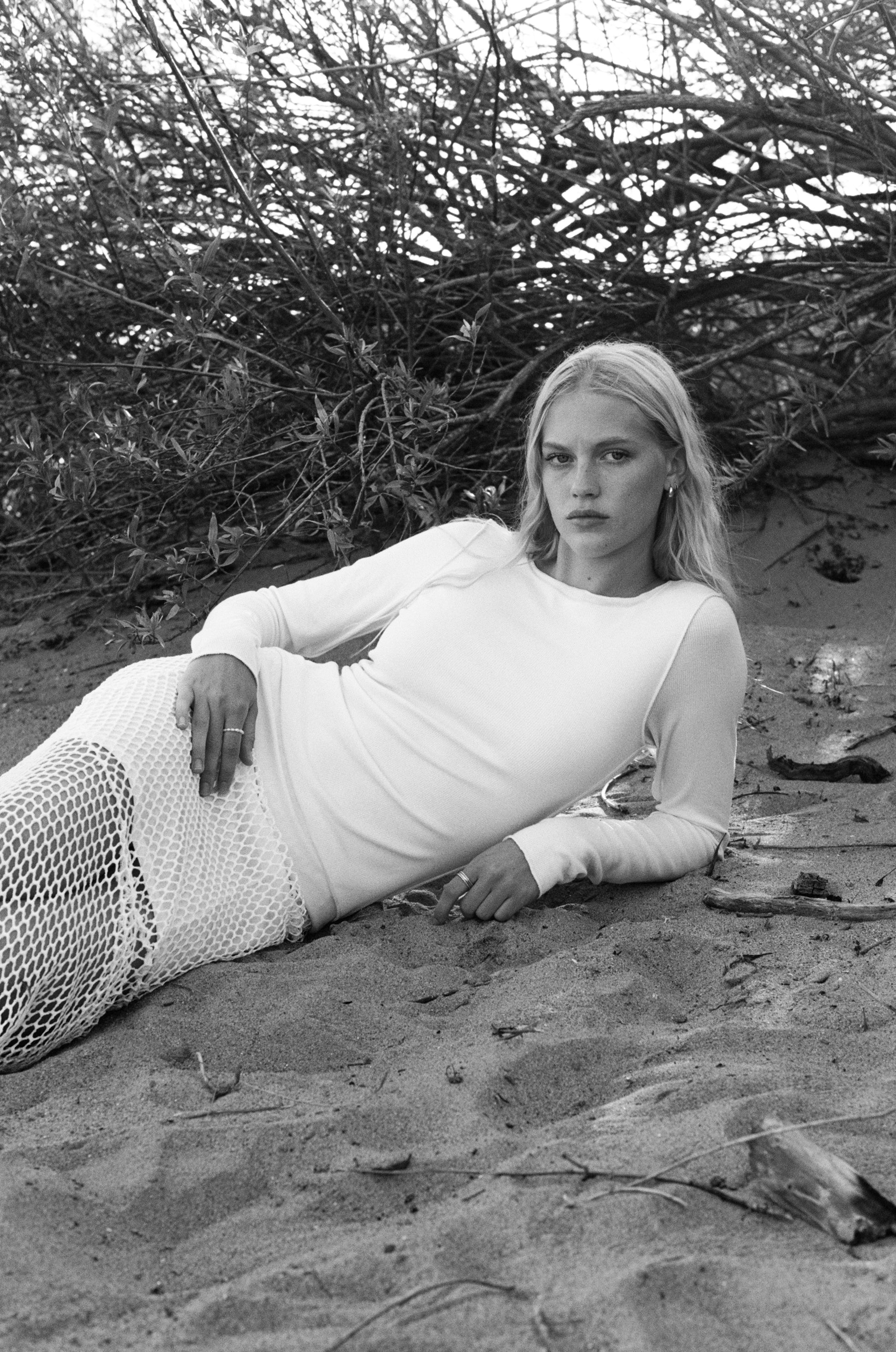 Female model wearing an exquisite crochet skirt featuring an asymmetrical silhouette in white paired with a modal knit long sleeve in white on the beach - VIR VITA
#color_coconut