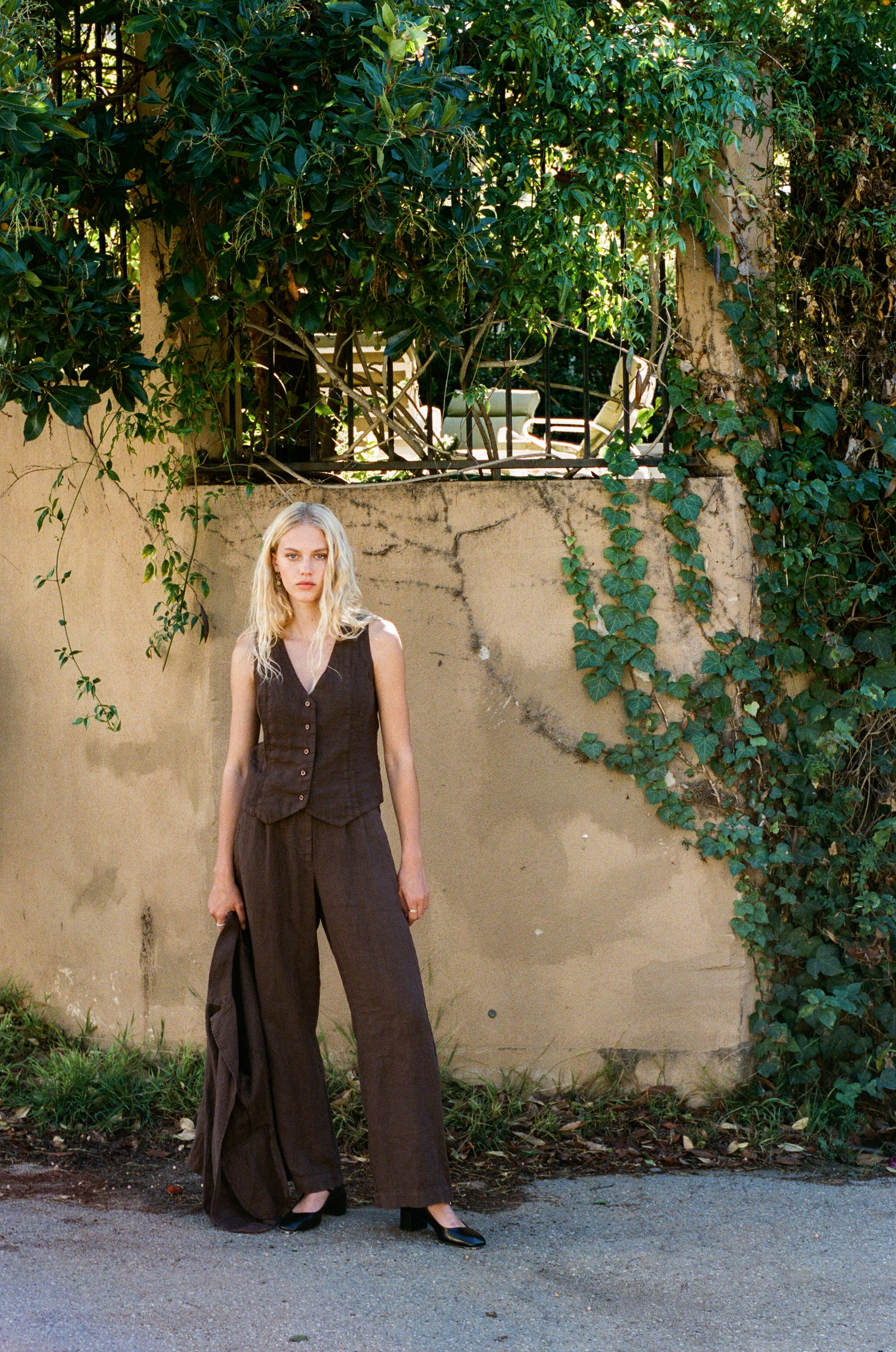 Female model wearing the 100% linen trouser featuring a high waisted double pleat silhouette in dark brown paired with a matching 100% linen blazer in dark brown and a 100% linen vest in dark brown - VIR VITA
#color_chestnut