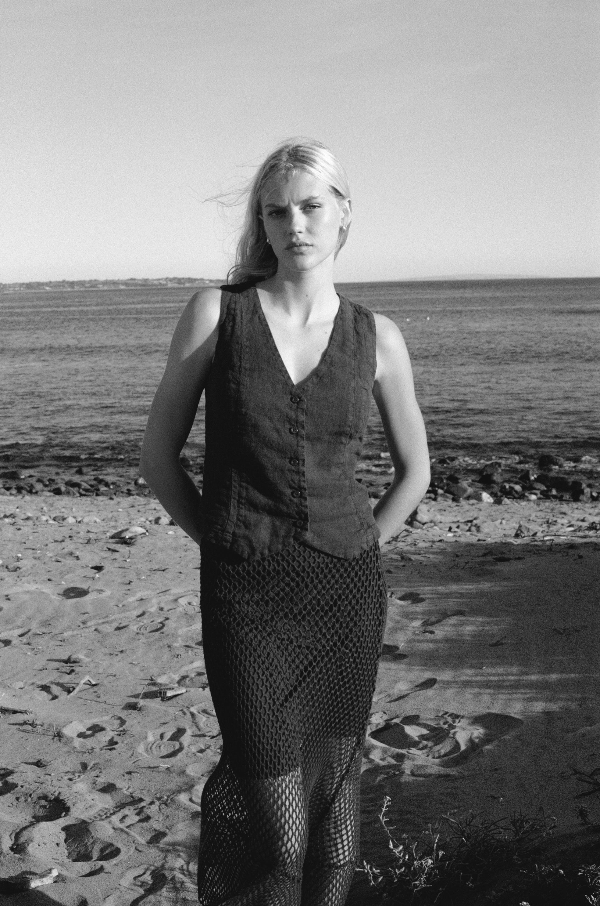 Female model wearing an exquisite crochet skirt featuring an asymmetrical silhouette in plum purple paired with a 100% linen vest in plum purple on the beach - VIR VITA
#color_plum