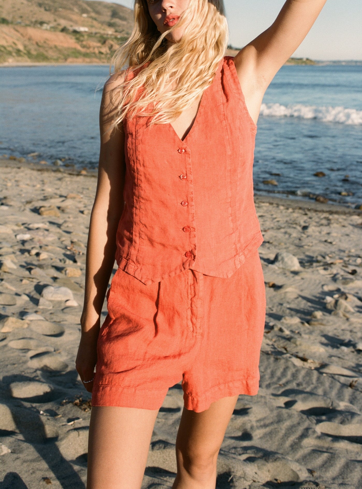 Female model wearing a sustainable 100% linen vest in orange with matching Italian handcrafted buttons paired with orange linen relaxed shorts on the beach - VIR VITA
#color_cayenne