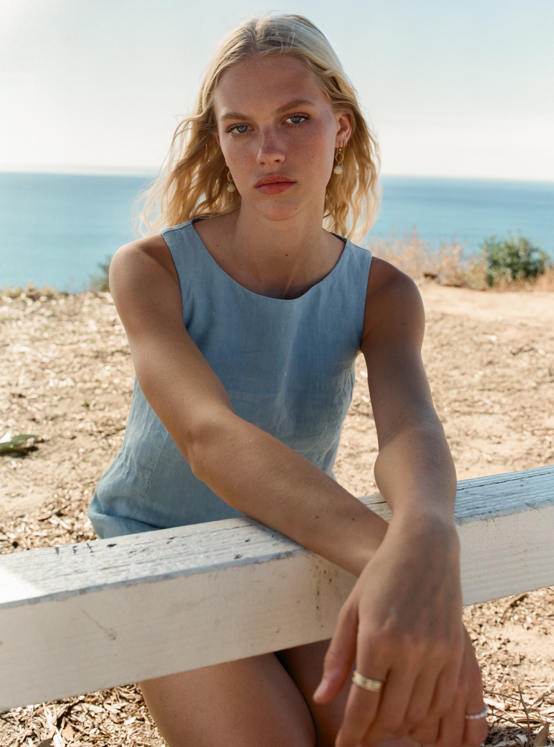 Female model wearing light blue 100% linen dress with a simple and comfortable silhouette overlooking the ocean - VIR VITA
#color_baby blue