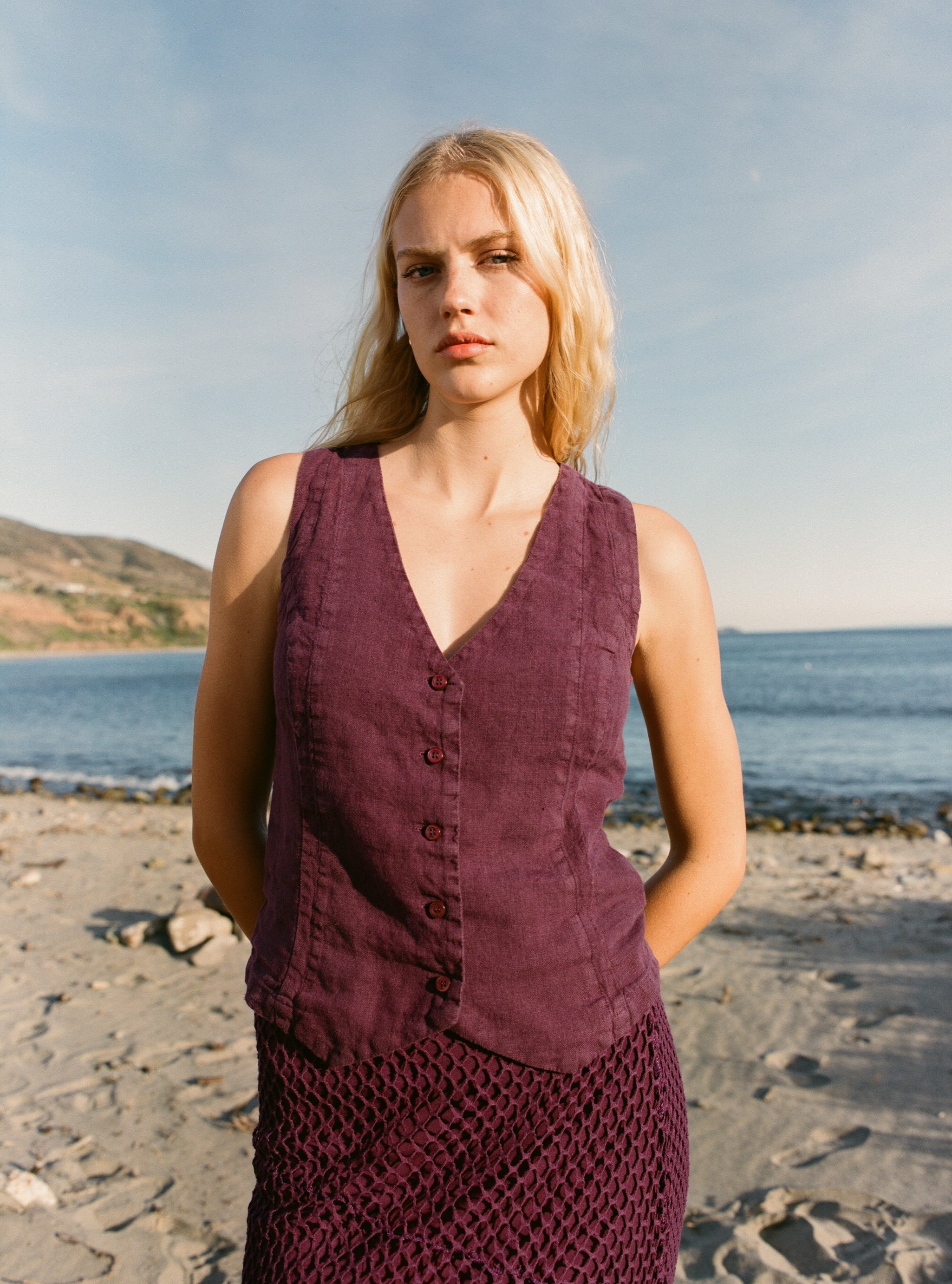 Female model wearing a plum purple 100% linen vest with matching Italian handcrafted buttons paired with a plum purple crochet skirt on the beach - VIR VITA
#color_plum
