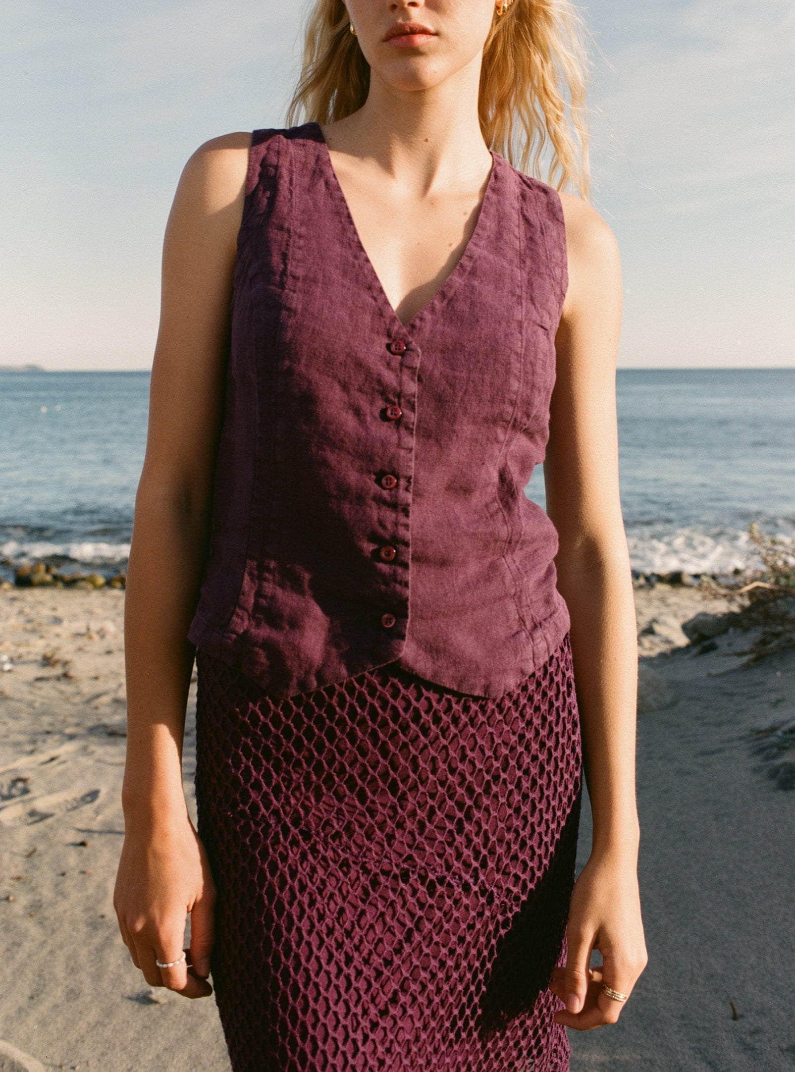Female model wearing a plum purple sustainable 100% linen vest with matching Italian handcrafted buttons paired with a plum purple crochet skirt on the beach - VIR VITA
#color_plum