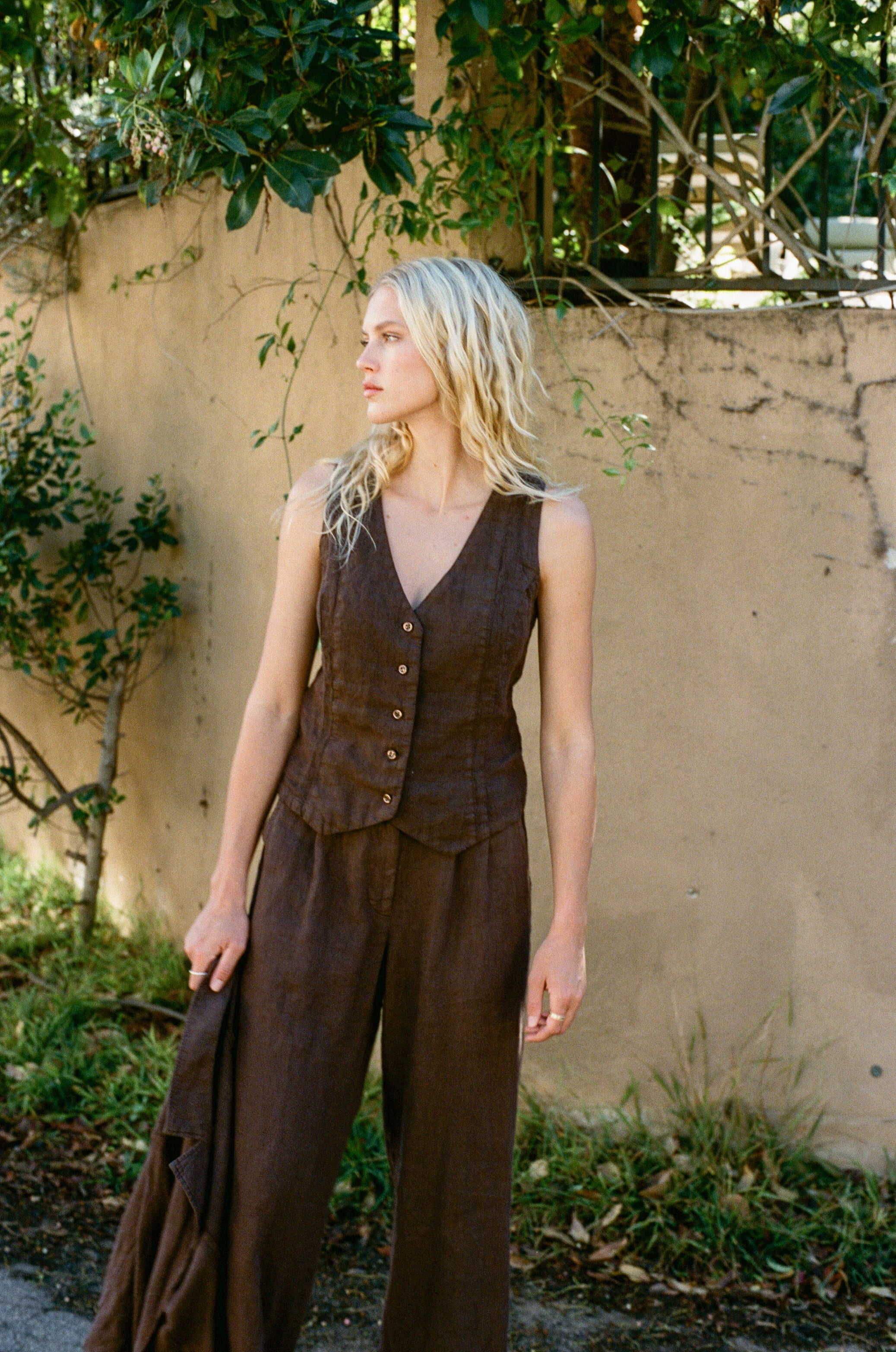 Female model wearing a dark brown sustainable 100% linen vest with matching Italian handcrafted buttons paired with dark brown linen trousers and a dark brown linen blazer - VIR VITA #color_chestnut