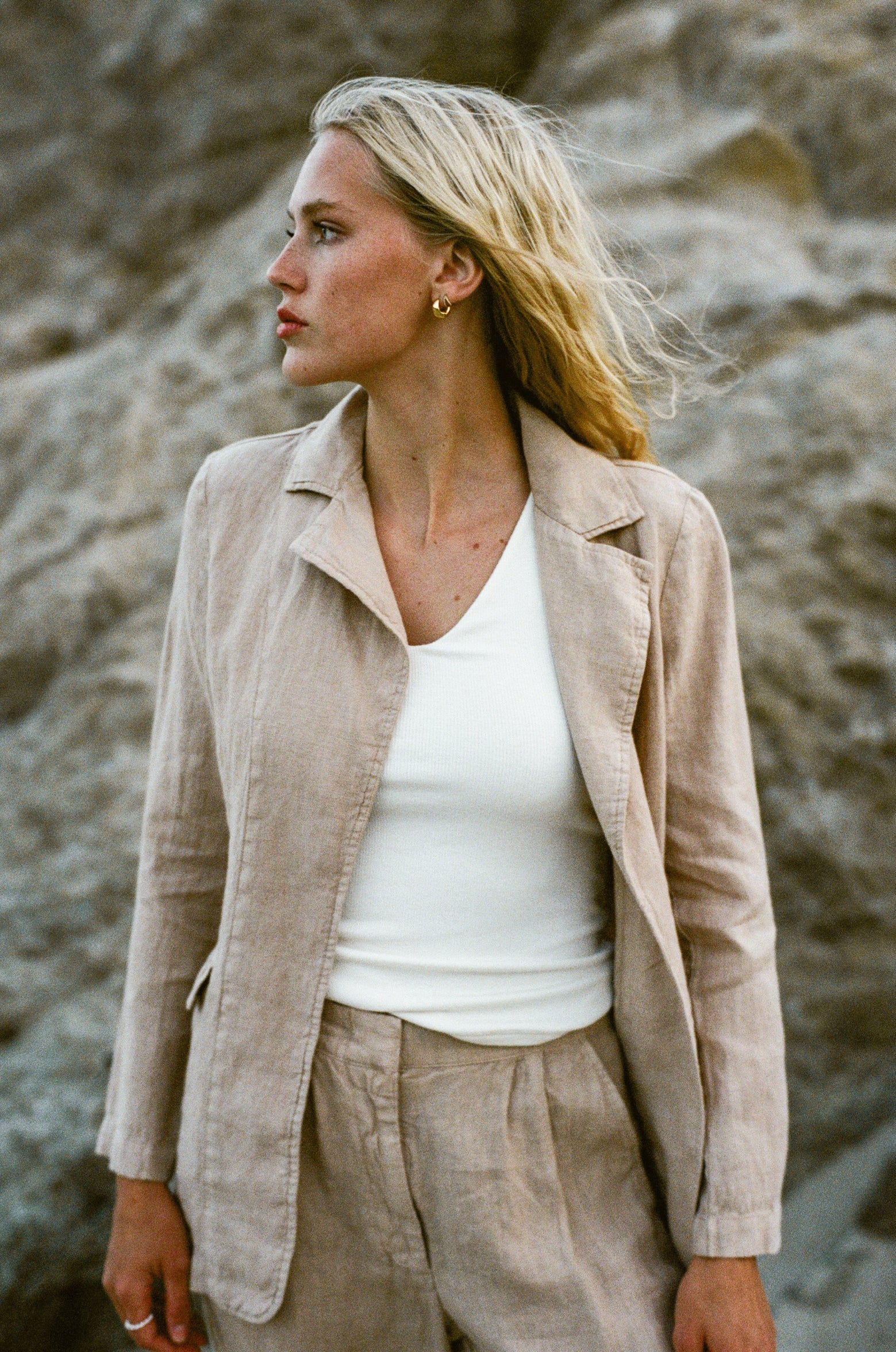 Female model wearing 100% linen blazer featuring an elegant and classic silhouette in beige paired with 100% linen matching trousers in beige and white modal tank top  at the beach -VIR VITA
#color_beige