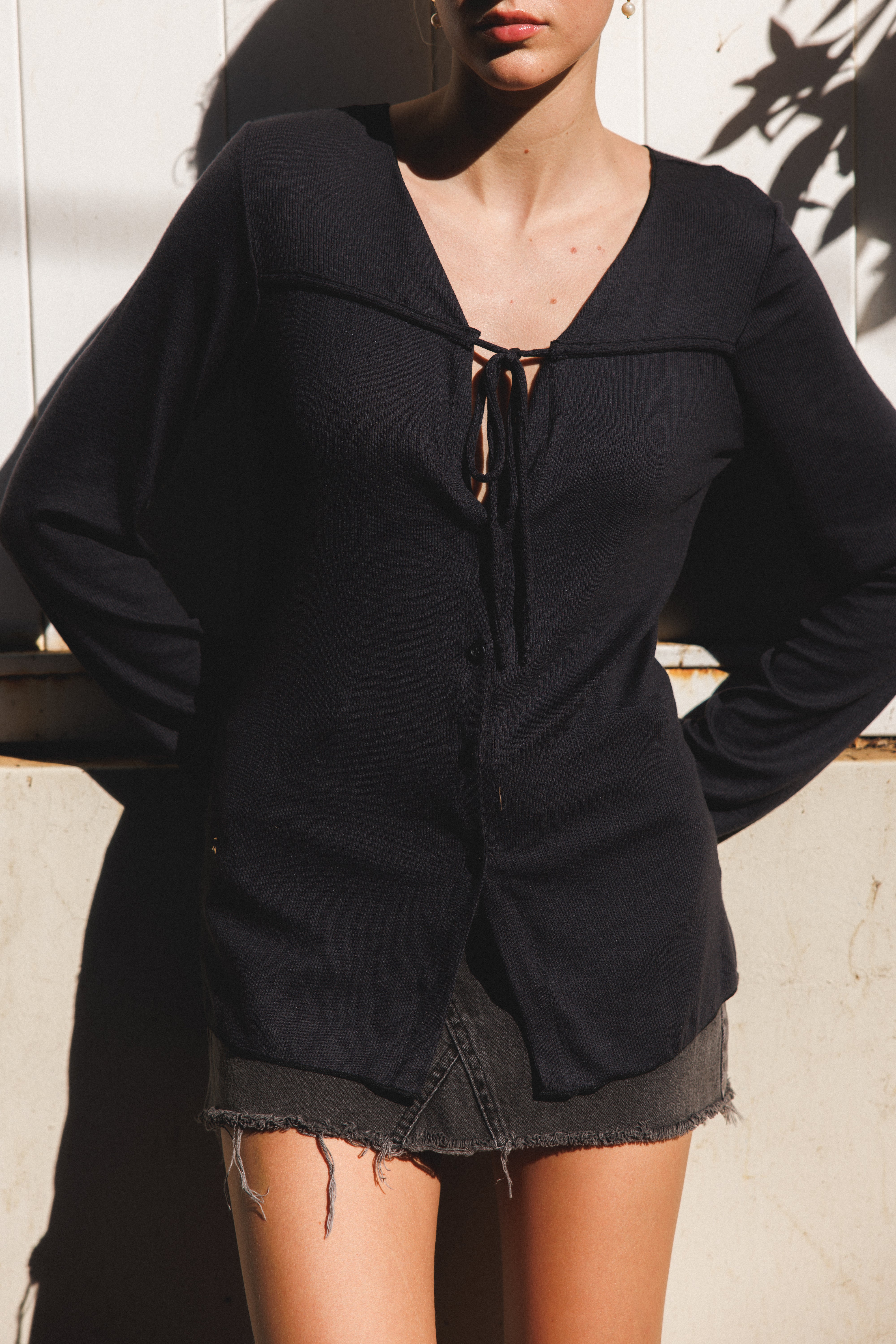 Female model wearing sustainable micro modal black buttery soft long sleeve ribbed top with tie and italian buttons and black mini skirt. Romantic top, Classic, timeless, elegant, french style. natural organic clothing- VIR VITA
#color_black