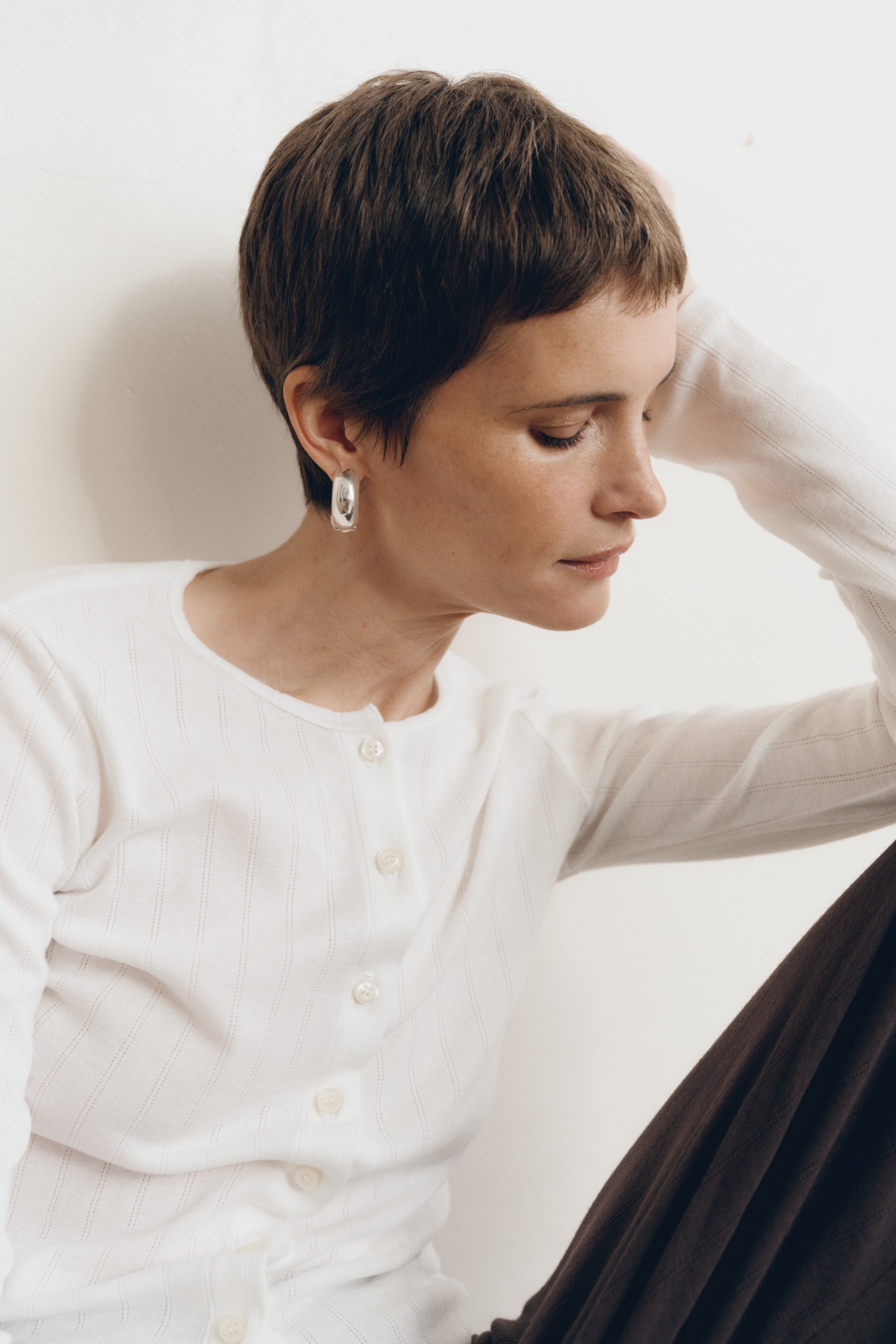 Posed female model wearing a button up sustainable 100% cotton pointelle knit cardigan in white paired with pointelle lounge pants in dark brown- VIR VITA
#color_coconut
