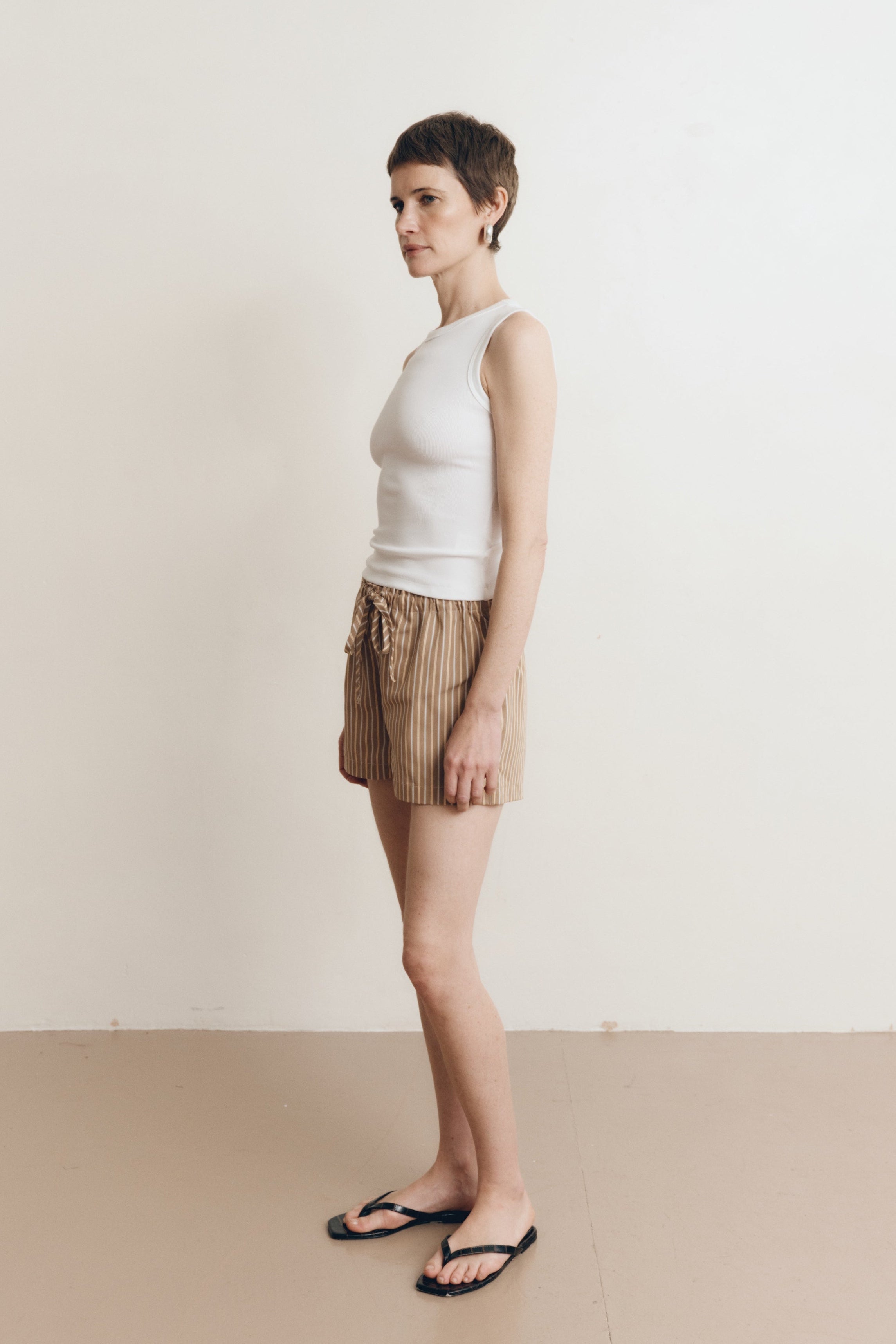 Posed female model wearing brown 100% cotton sustainable drawstring relaxed shorts paired with a high neck tank top in white and black sandals - VIR VITA
#color_canyon stripe