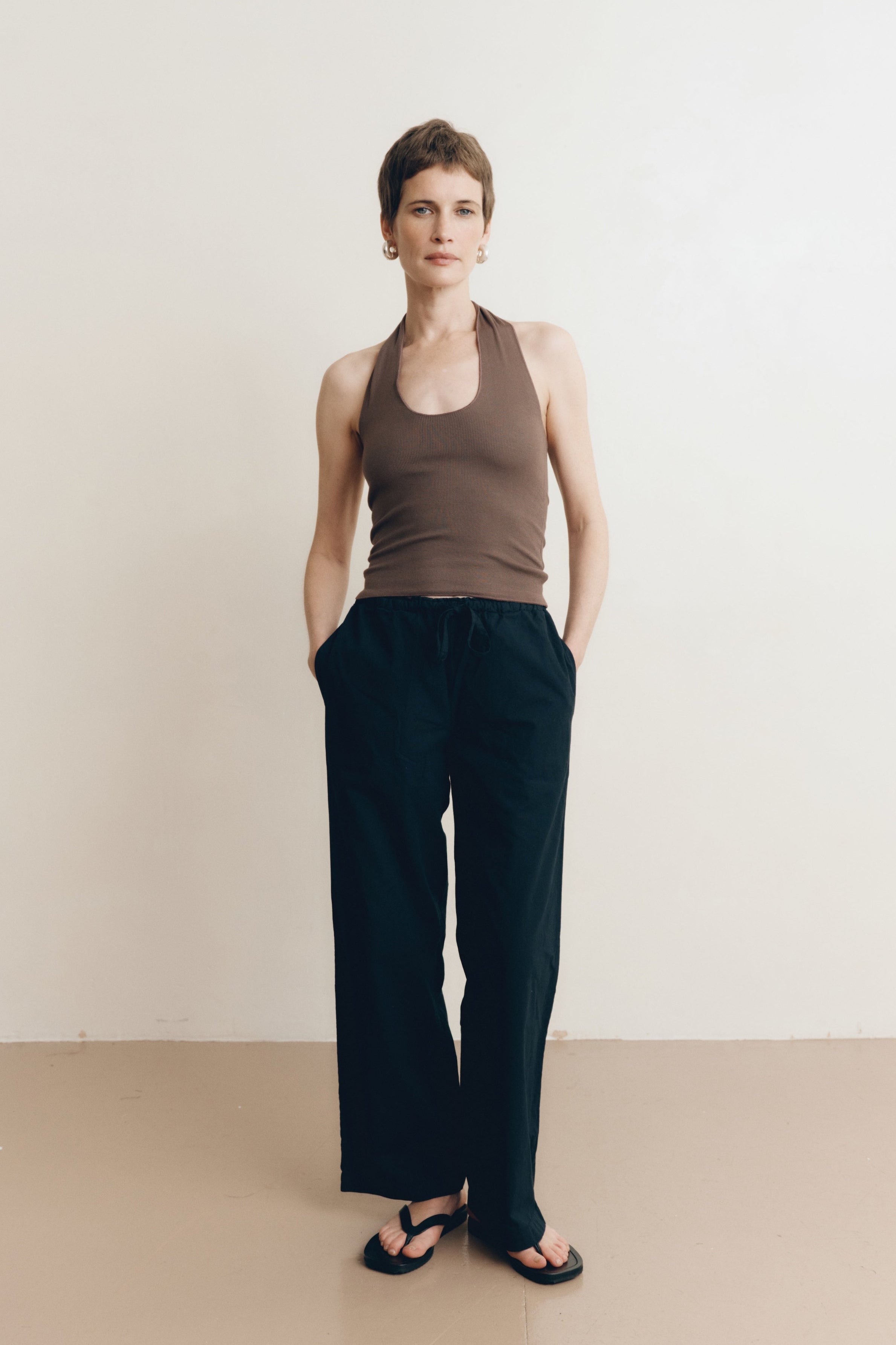 Posed female model wearing 100% cotton poplin drawstring relaxed pants in black paired with a modal dark brown halter top and black sandals - VIR VITA
#color_black