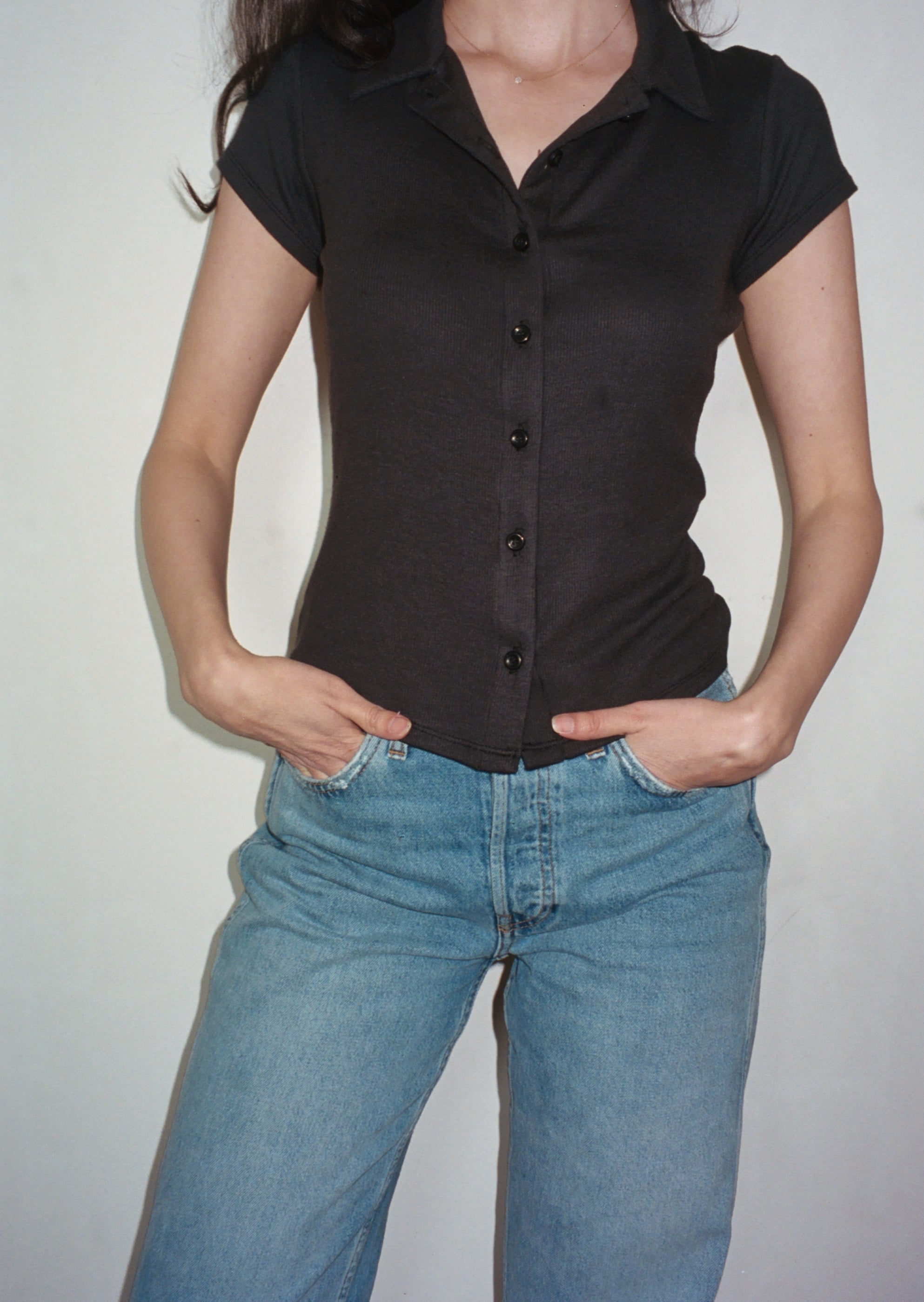 Female model wearing black sustainable micro modal short sleeve ribbed polo top with italian button detailing. Classic, timeless, elegant, french style. Natural organic clothing - VIR VITA

#color_black