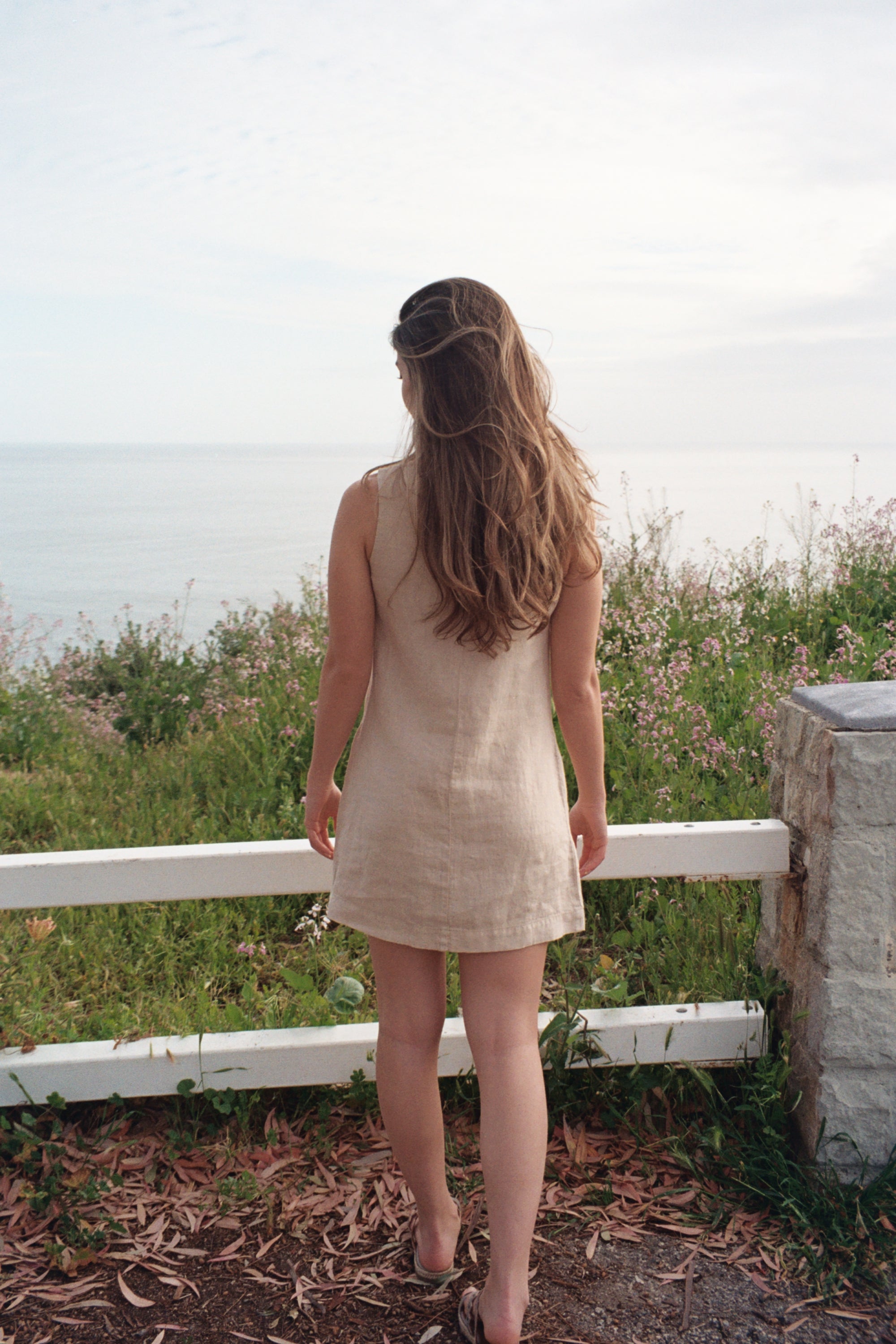 
female model wearing sustainable beige linen dress overlooking the ocean- VIR VITA
#color_beige