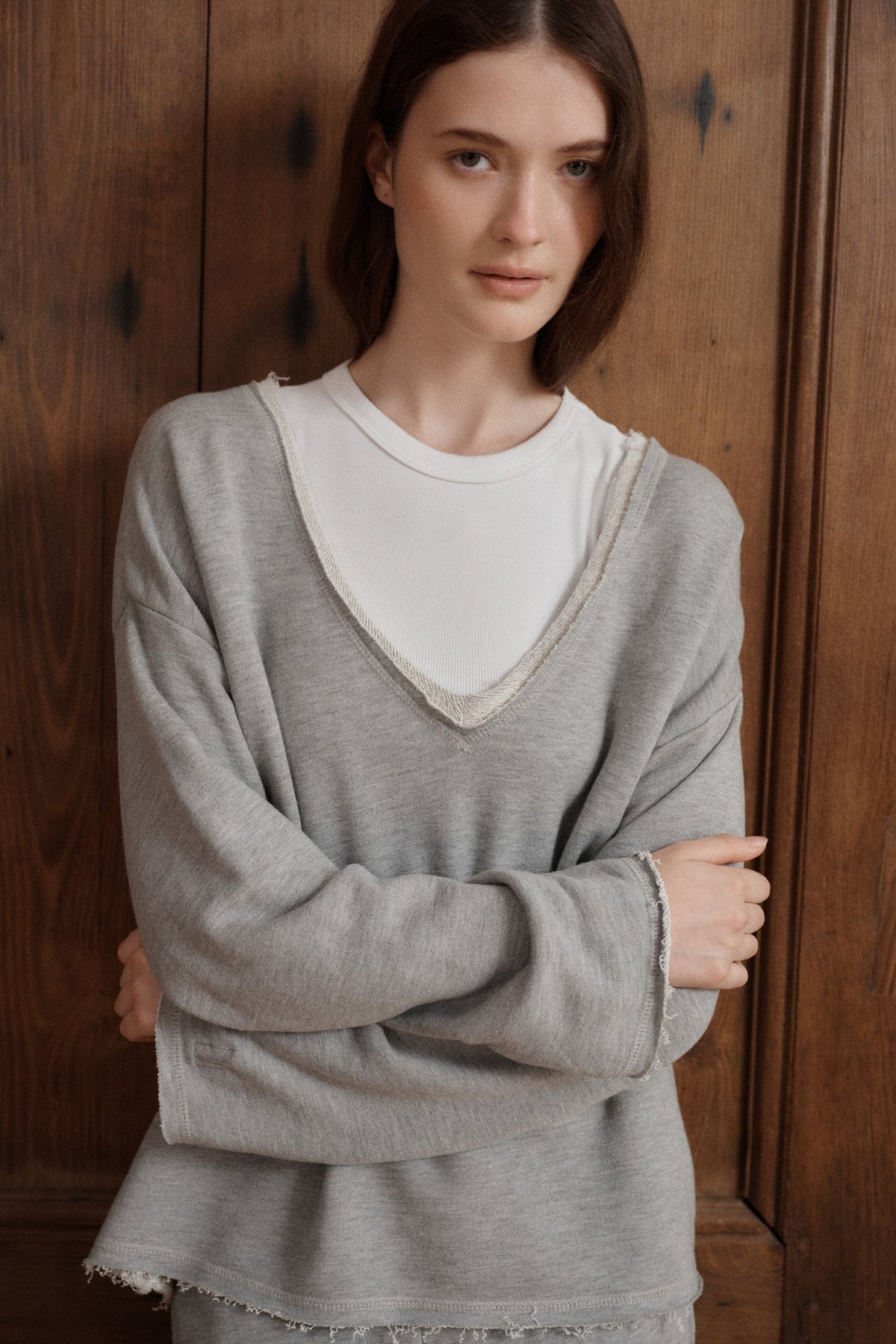 Female model posing wearing a v-neck heather grey relaxed sweatshirt featuring a raw hem paired with heather grey joggers and a white high neck tank top underneath. - VIR VITA
#color_heather grey