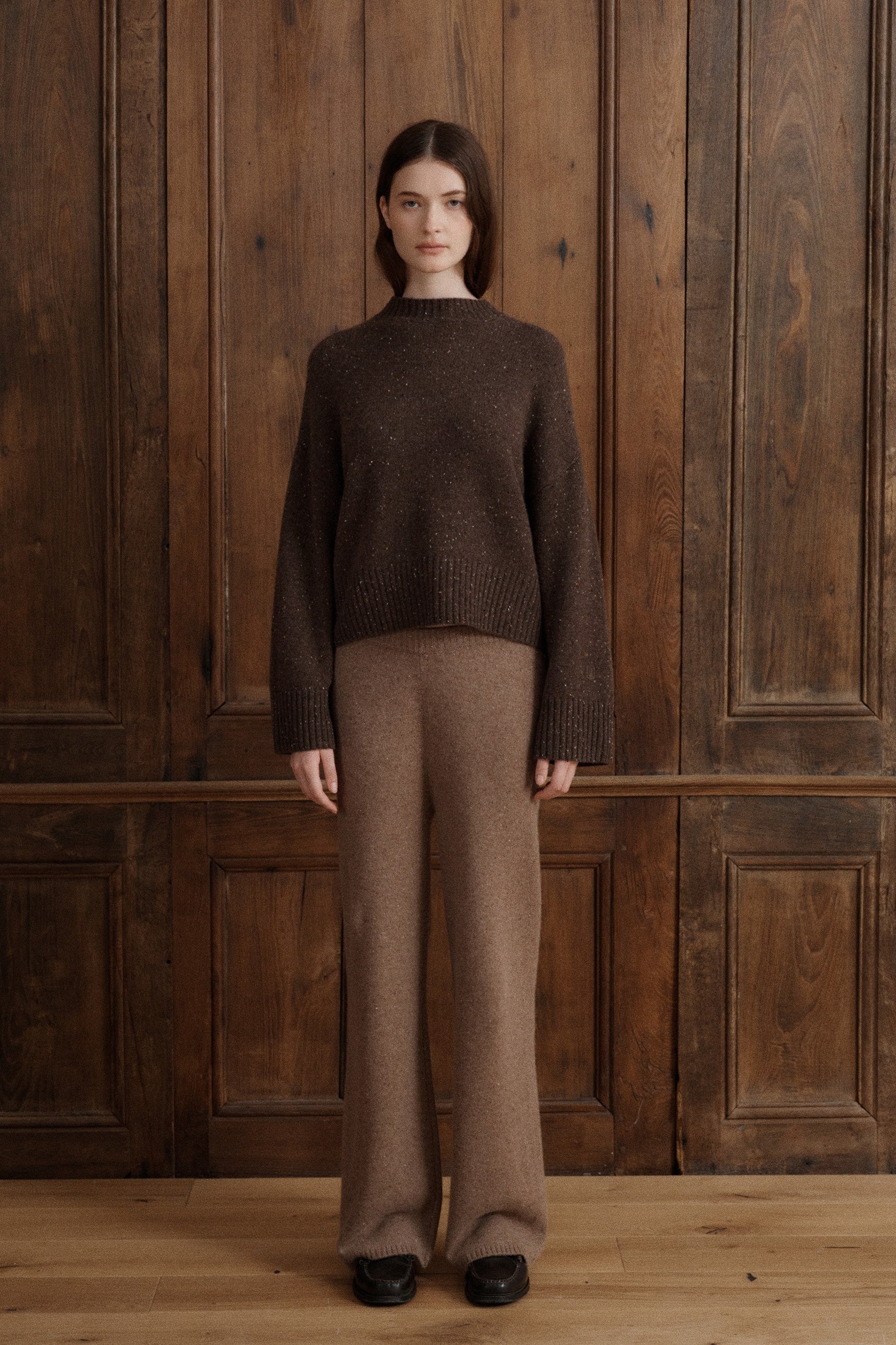 Female model wearing a classic mock neck cashmere sweater in dark brown. Knit from grade A cashmere with wide balloon sleeves and dropped shoulders for an effortless silhouette. The sweater is paired with cashmere lounge pants in a light brown. -VIR VITA
#color_oak