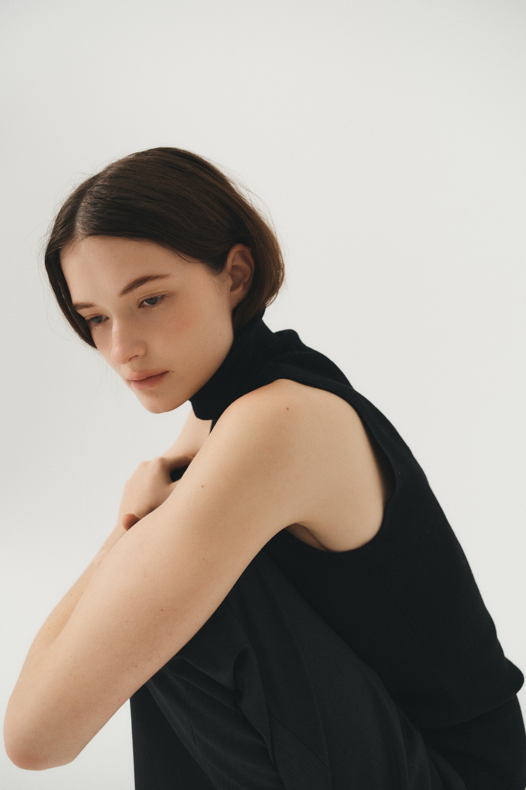 Female model wearing a black fitted sleeveless turtleneck crafted from a fine wool, cashmere and silk blend. Paired with elastic waist wool trousers in dark grey - VIR VITA
#color_black