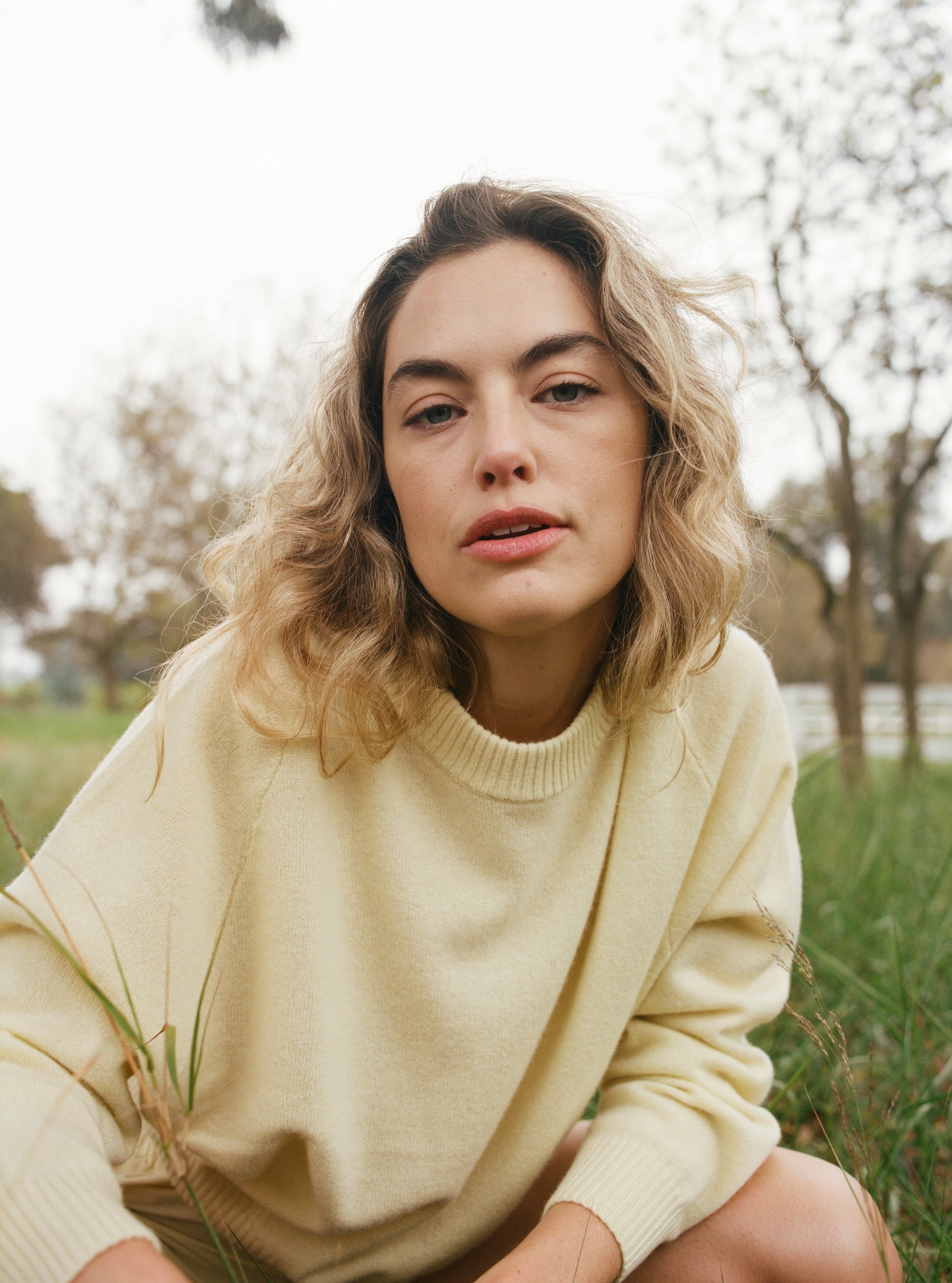 Female model in a field wearing a pale yellow luxurious and soft cashmere pullover sweater with a classic and relaxed silhouette - VIR VITA
#color_butter