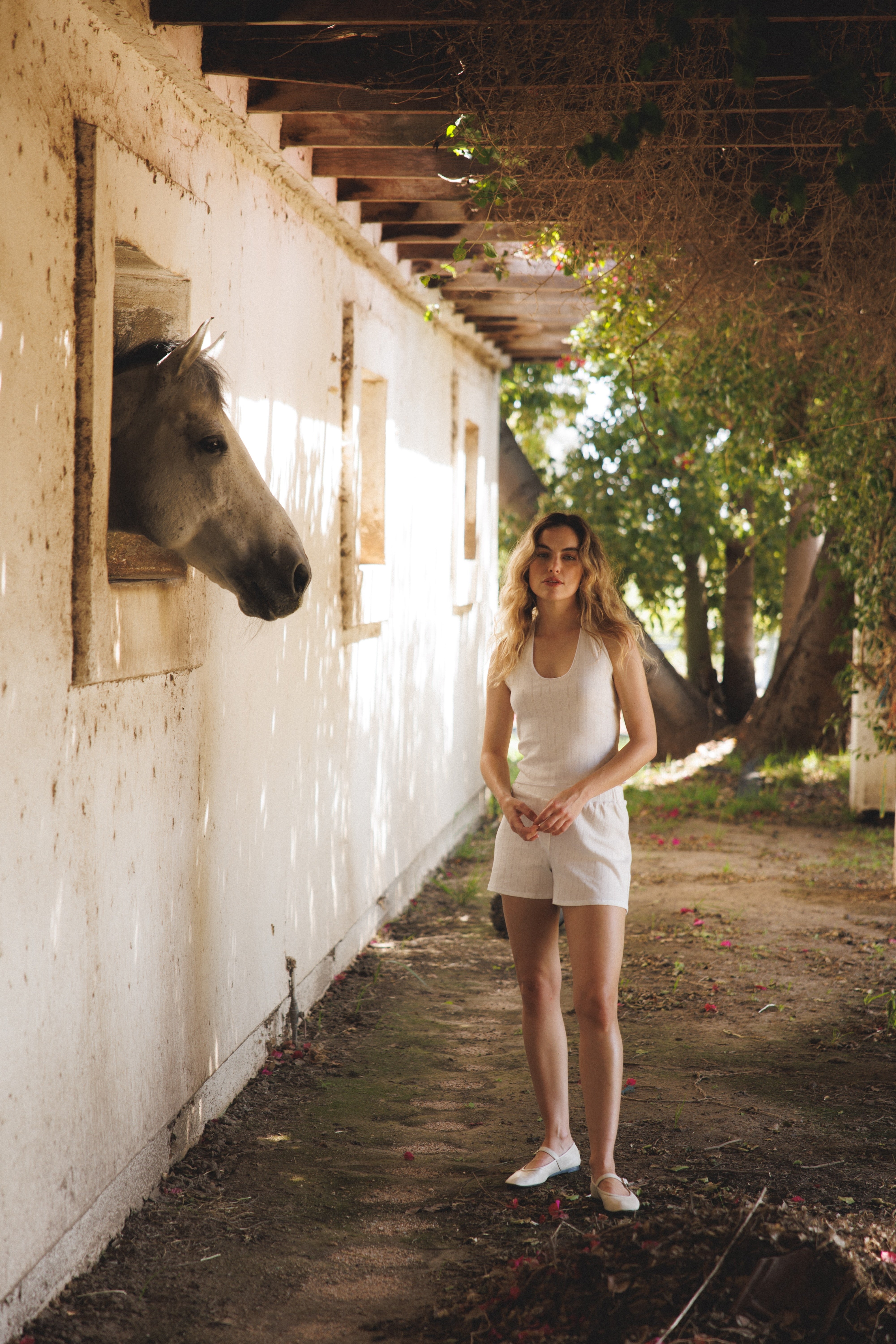 Female model wearing sustainable white pointelle lounge shorts made of 100% recycled cotton featuring a relaxed fit paired with a matching pointelle halter top in white and white flats - VIR VITA 
#color_coconut