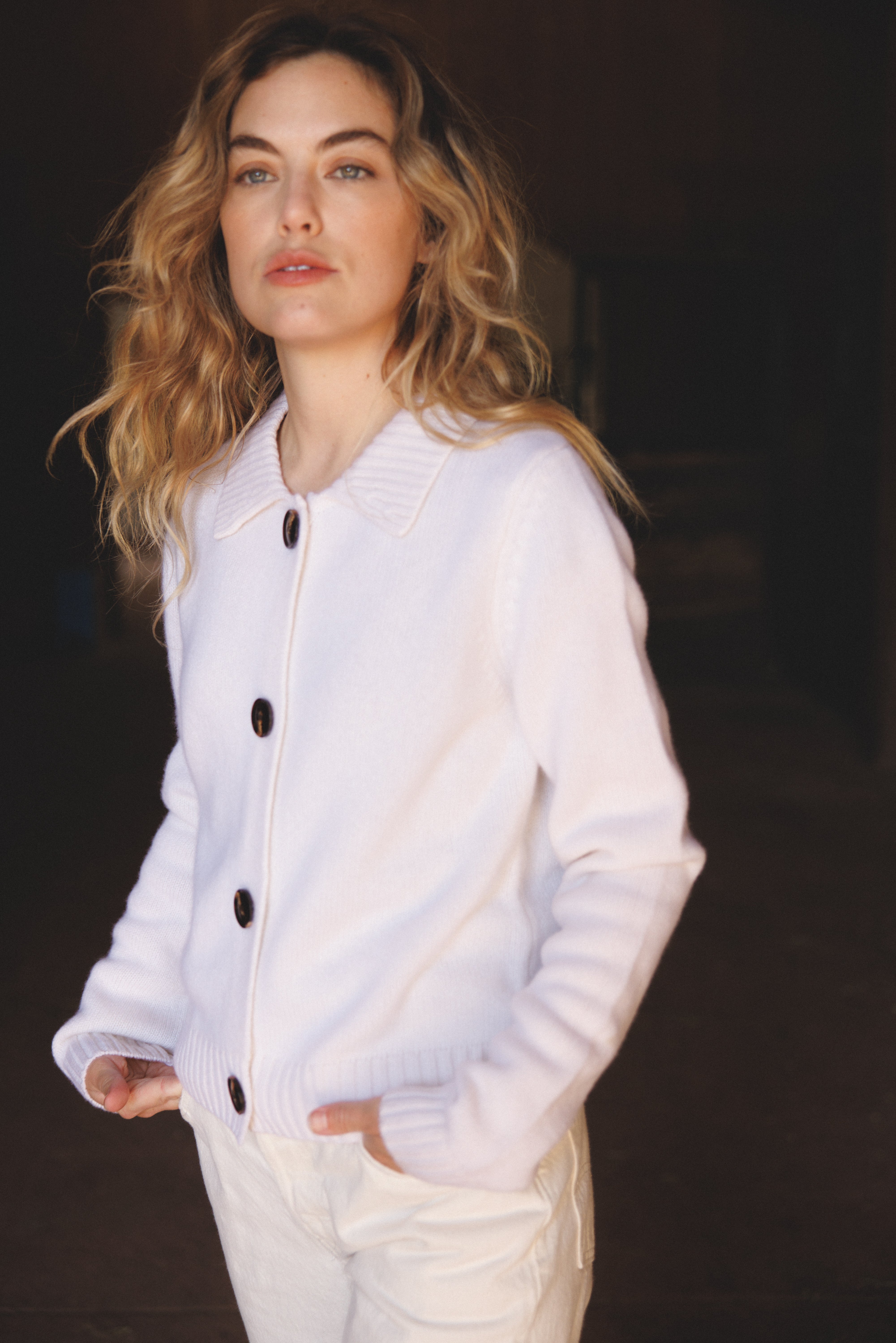 Female model wearing a white ultra-soft luxurious cashmere cardigan featuring a classic silhouette with a collar and large buttons paired with white jeans - VIR VITA
#color_bone